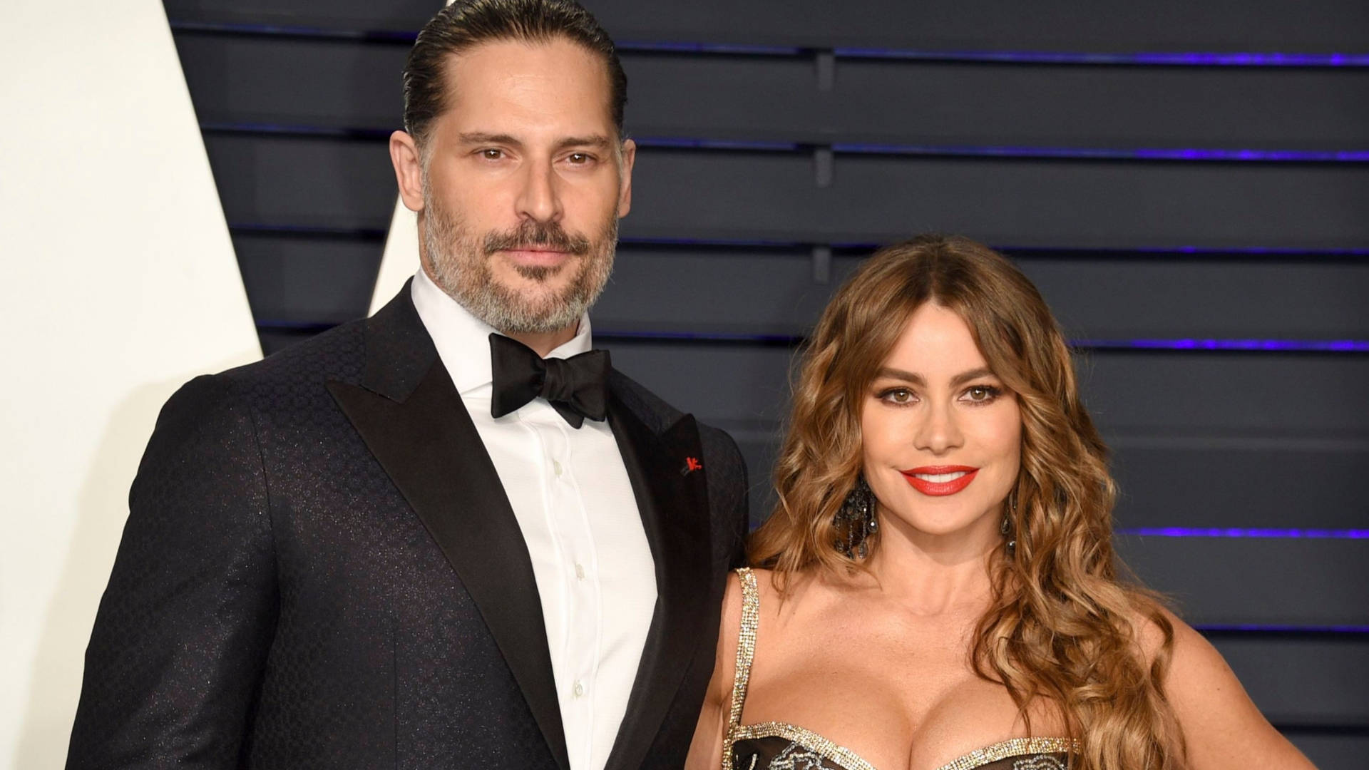 Sofia Vergara 桌布 壁紙 — 一對魅力情侶在紅地毯活動中擺姿勢，穿著優雅的正式服裝，背景是時尚的藍色燈光。