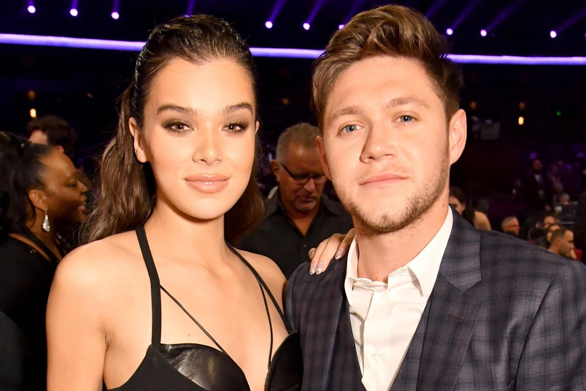 Hailee Steinfeld 桌布 壁紙 — 一對魅力情侶在紫色舞台燈光下，於一場耀眼活動中合照，身後有群眾。