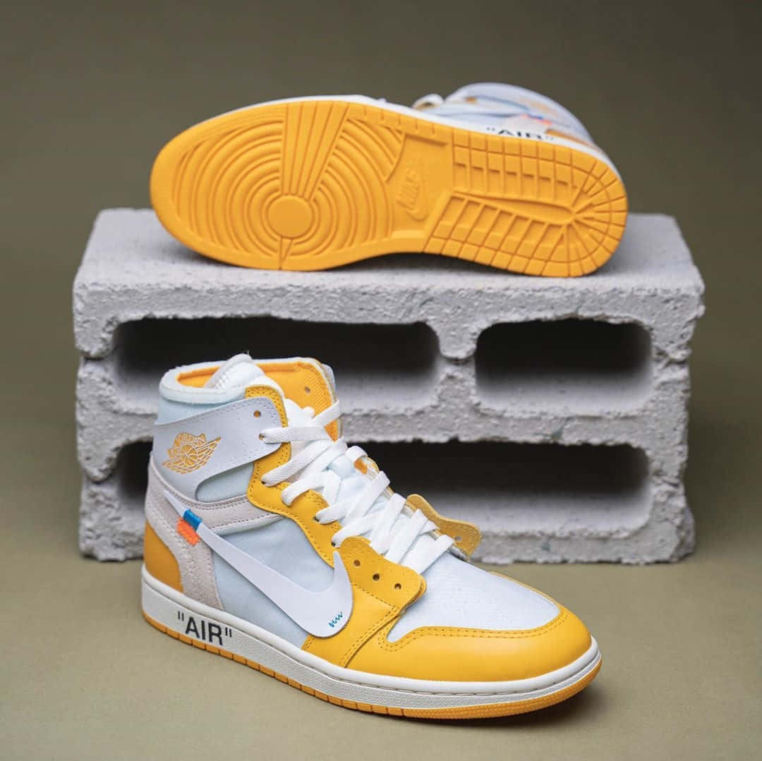 Off White Jordan 1 桌布 壁紙 — 一對黃白相間的高筒運動鞋，鞋底可見，放在灰色混凝土塊上，背景柔和。