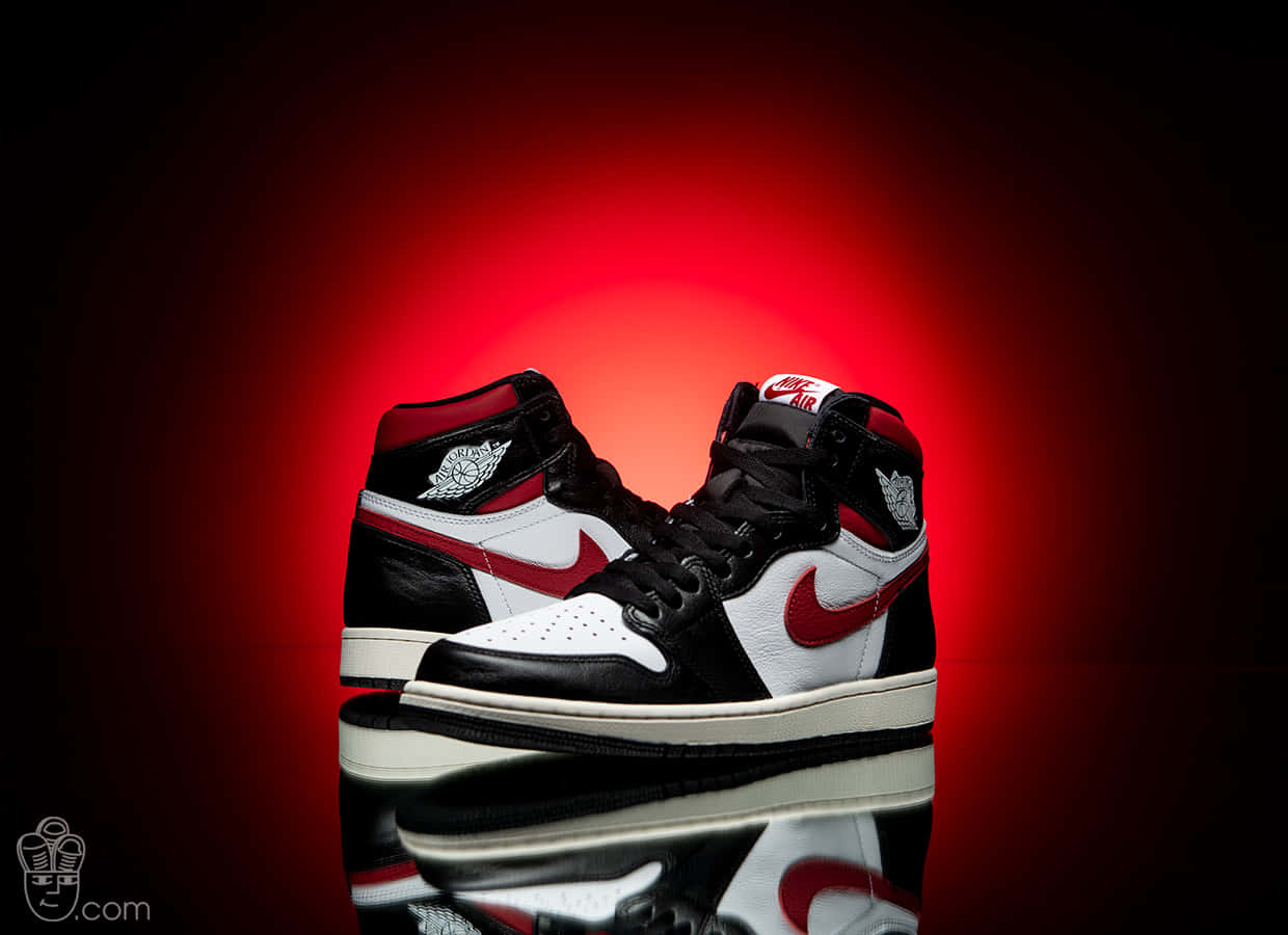 Air Jordan 1 桌布 壁紙 — 一對黑、白、紅色的 Air Jordan 1 運動鞋在反光表面上，於耀眼的紅色聚光燈下閃閃發光。