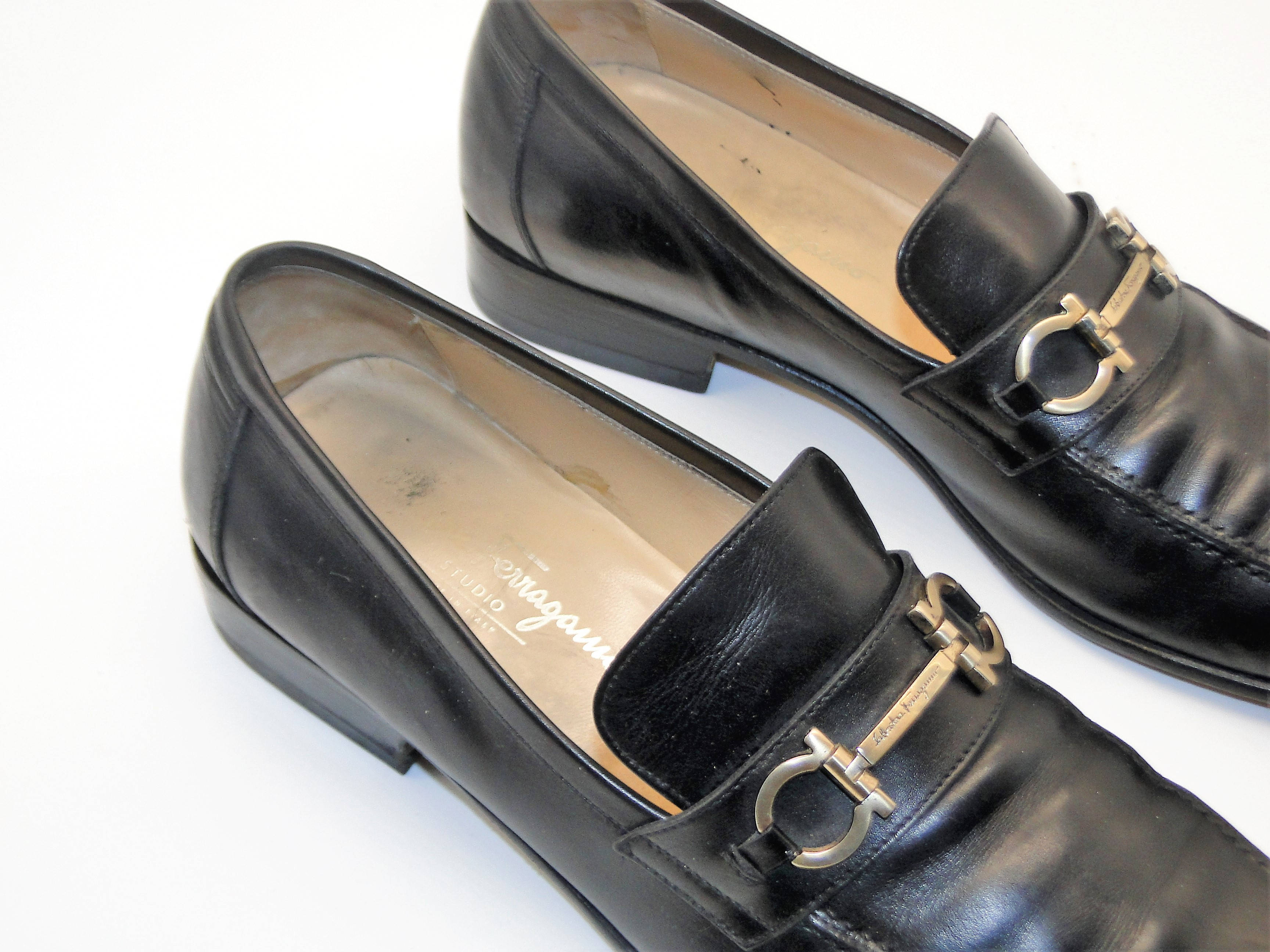Ferragamo 桌布 壁紙 — 一對黑色皮革樂福鞋，帶有金色馬銜扣細節，放在乾淨的白色背景上。