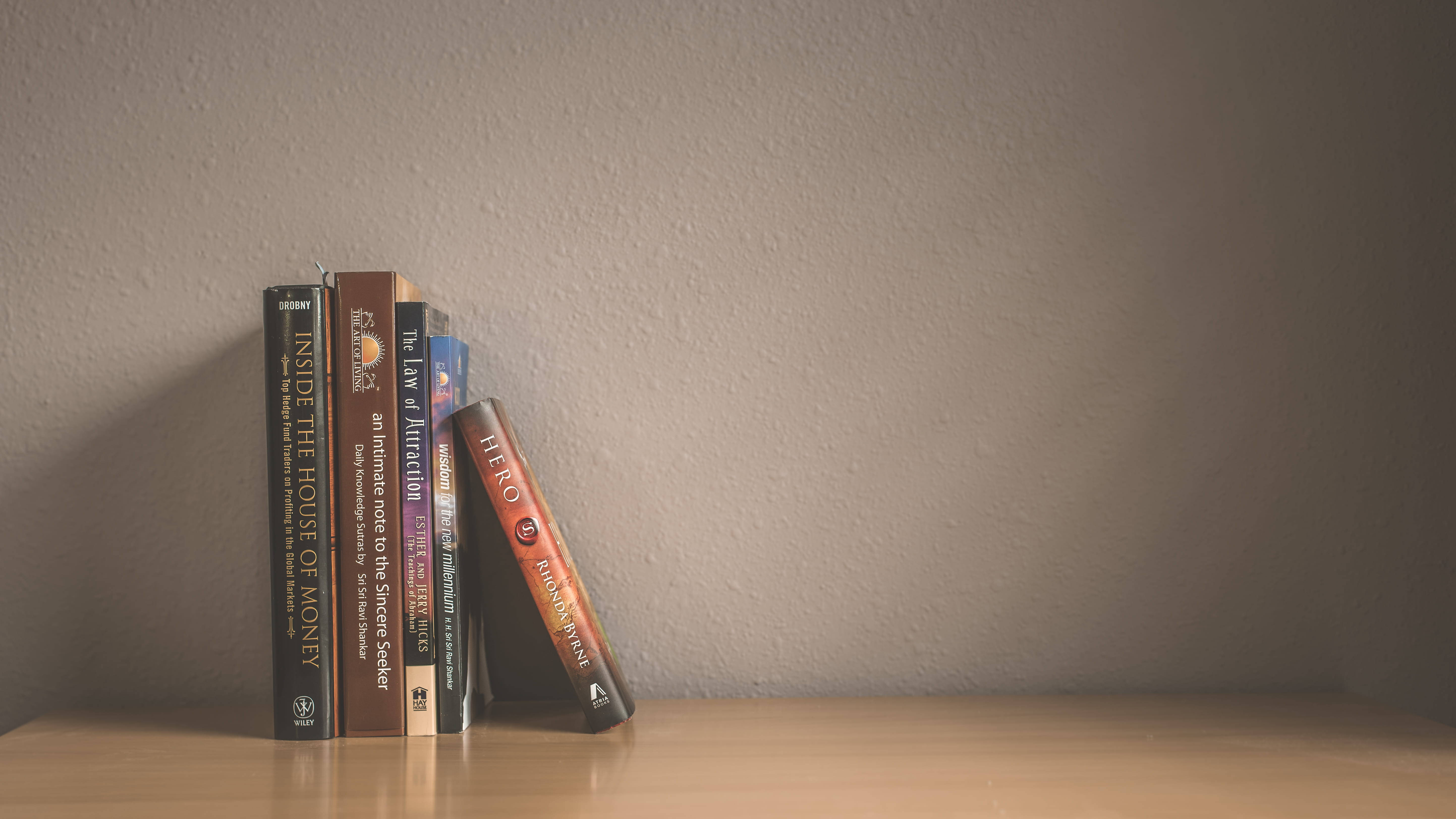 Bookshelf 桌布 壁紙 — 一小疊勵志和理財書籍靠在有紋理的牆壁上，放在木架子上，柔和自然光線。