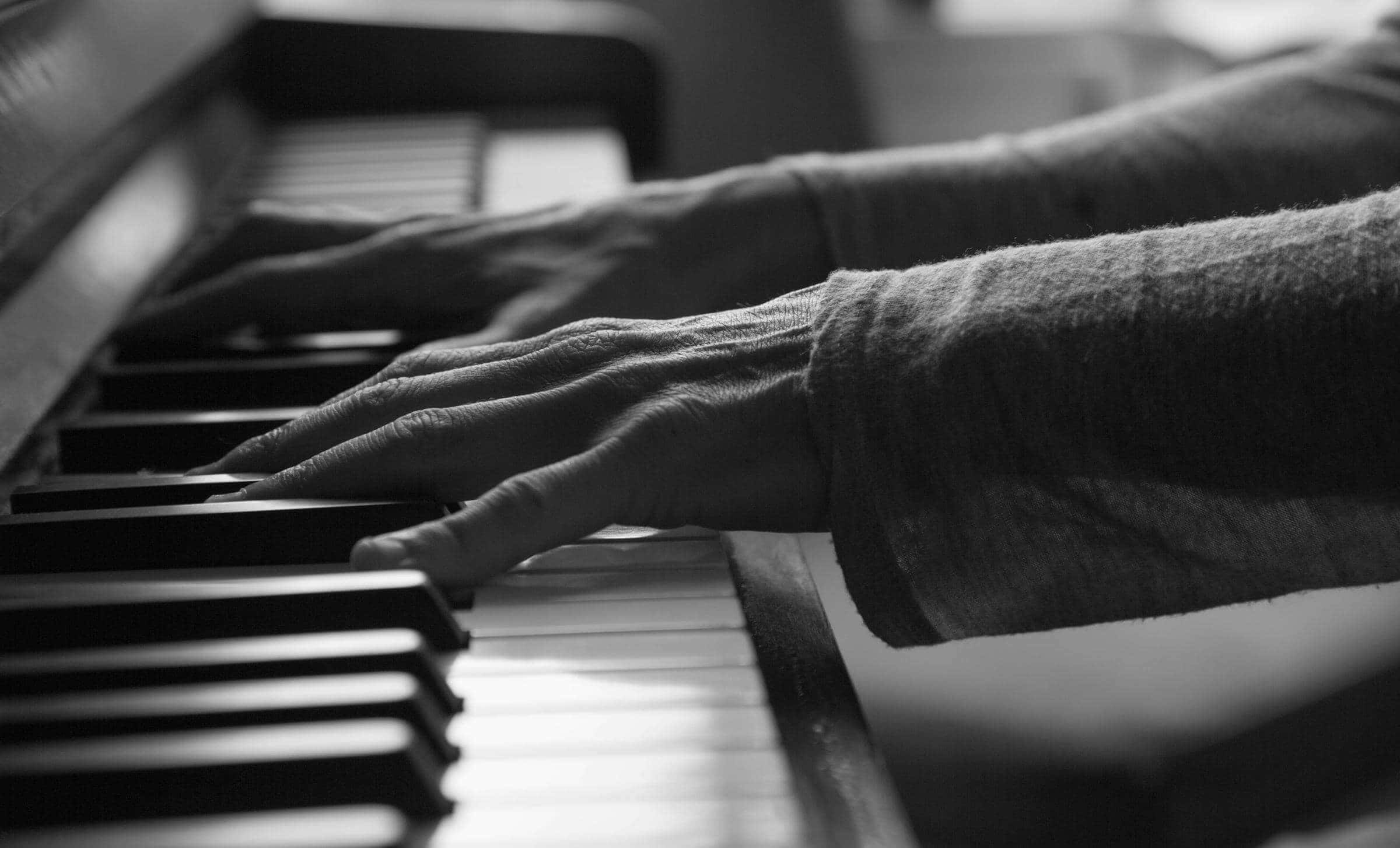 Black And White Piano 桌布 壁紙 — 一幀黑白特寫，雙手在柔和燈光下優雅地彈奏鋼琴琴鍵。