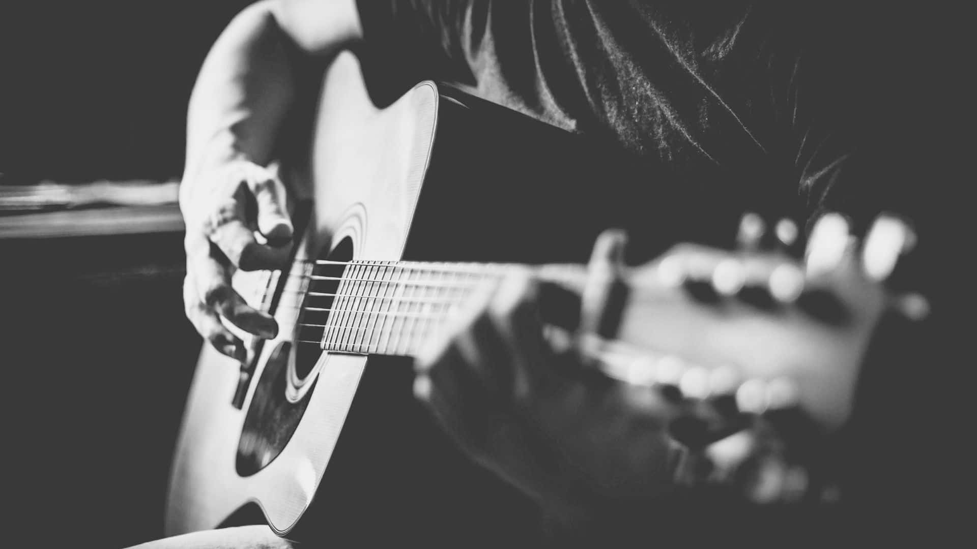Black And White Guitar 桌布 壁紙 — 一幀黑白特寫，雙手彈奏木吉他，景深較淺。
