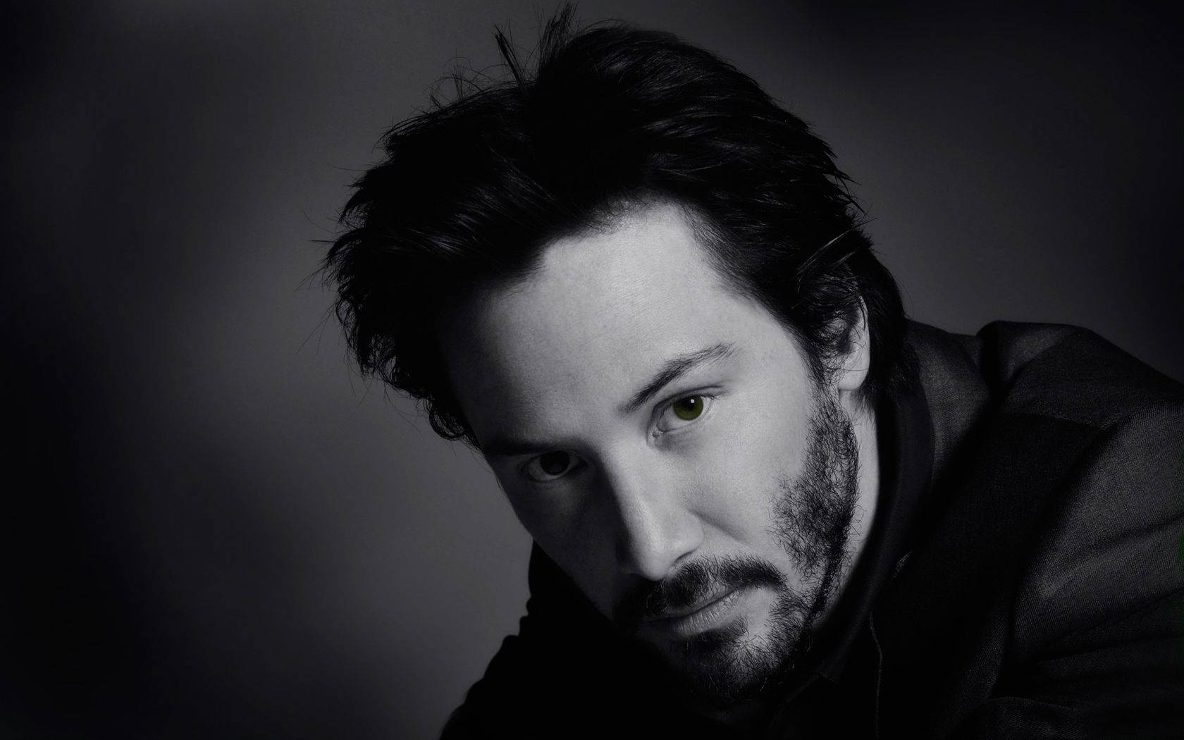 Keanu 桌布 壁紙 — 一幅充滿情緒的黑白肖像，一名男子擁有強烈的綠色眼睛，直視觀眾，背景為深色漸變。