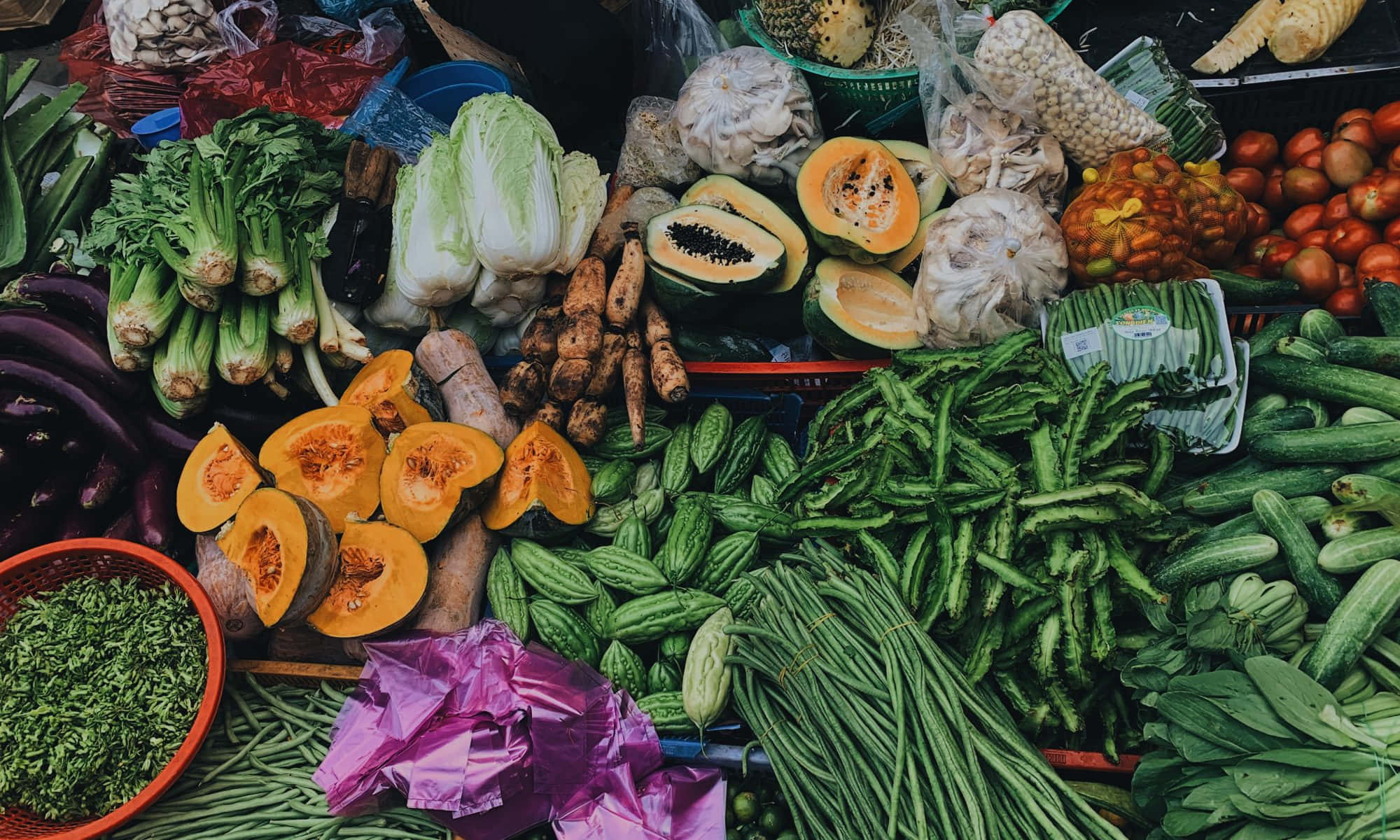 Vegetables 桌布 壁紙 — 一幅充滿活力的俯瞰圖，展示一個熙熙攘攘的市場攤位，堆滿了色彩繽紛的新鮮農產品，包括青豆、小黃瓜、番茄和木瓜。