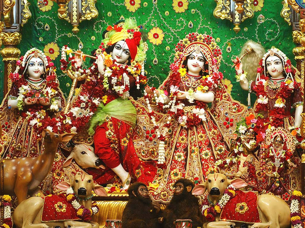 Iskcon 桌布 壁紙 — 一幅充滿活力的印度教神靈場景，克里希納吹奏長笛，周圍有女神、鹿和猴子，裝飾著紅色、金色和花環。