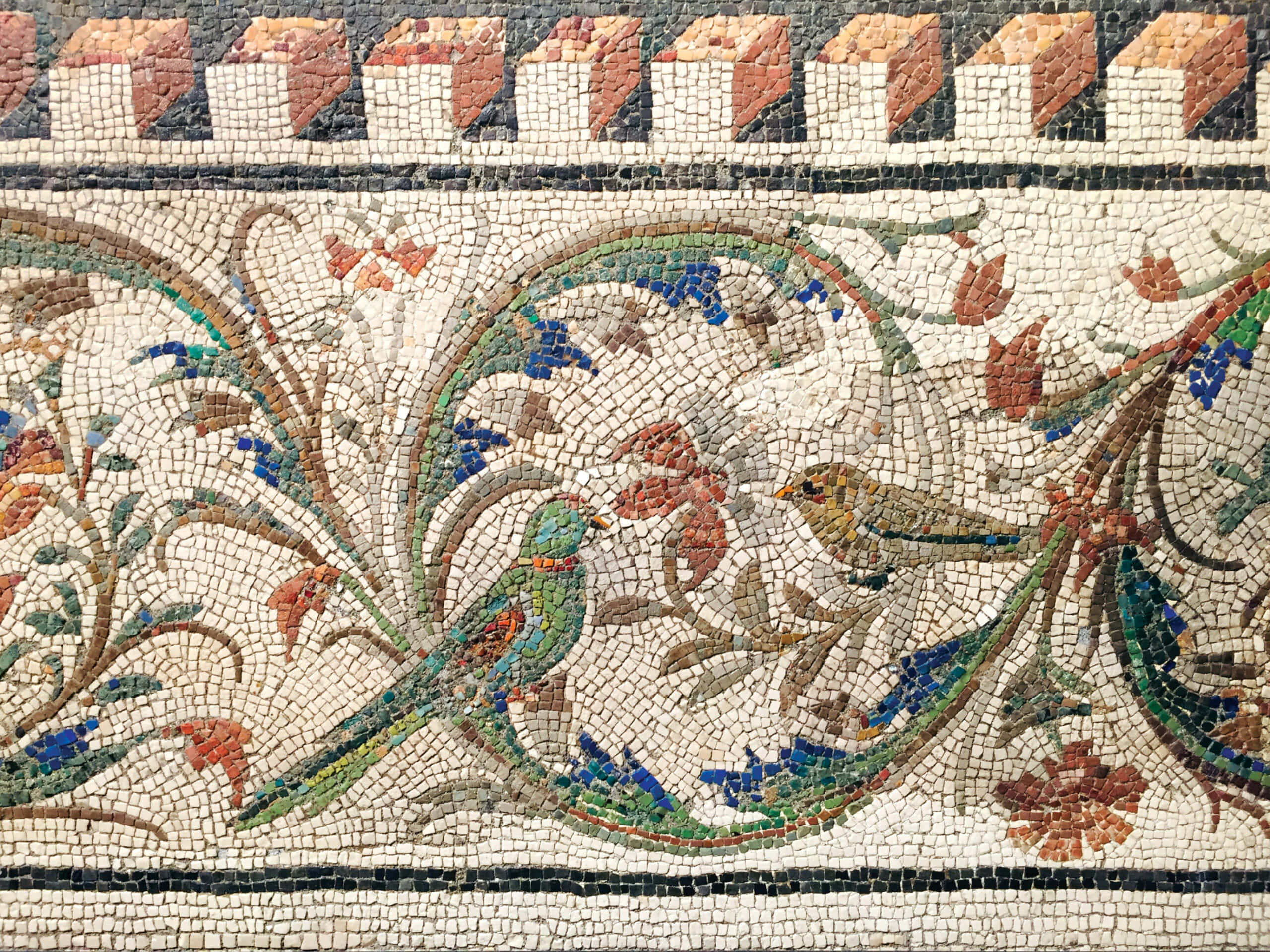 Mosaic 桌布 壁紙 — 一幅充滿活力的古代馬賽克描繪了兩隻色彩繽紛的鳥兒棲息在帶有幾何邊框圖案的旋轉花卉藤蔓中。
