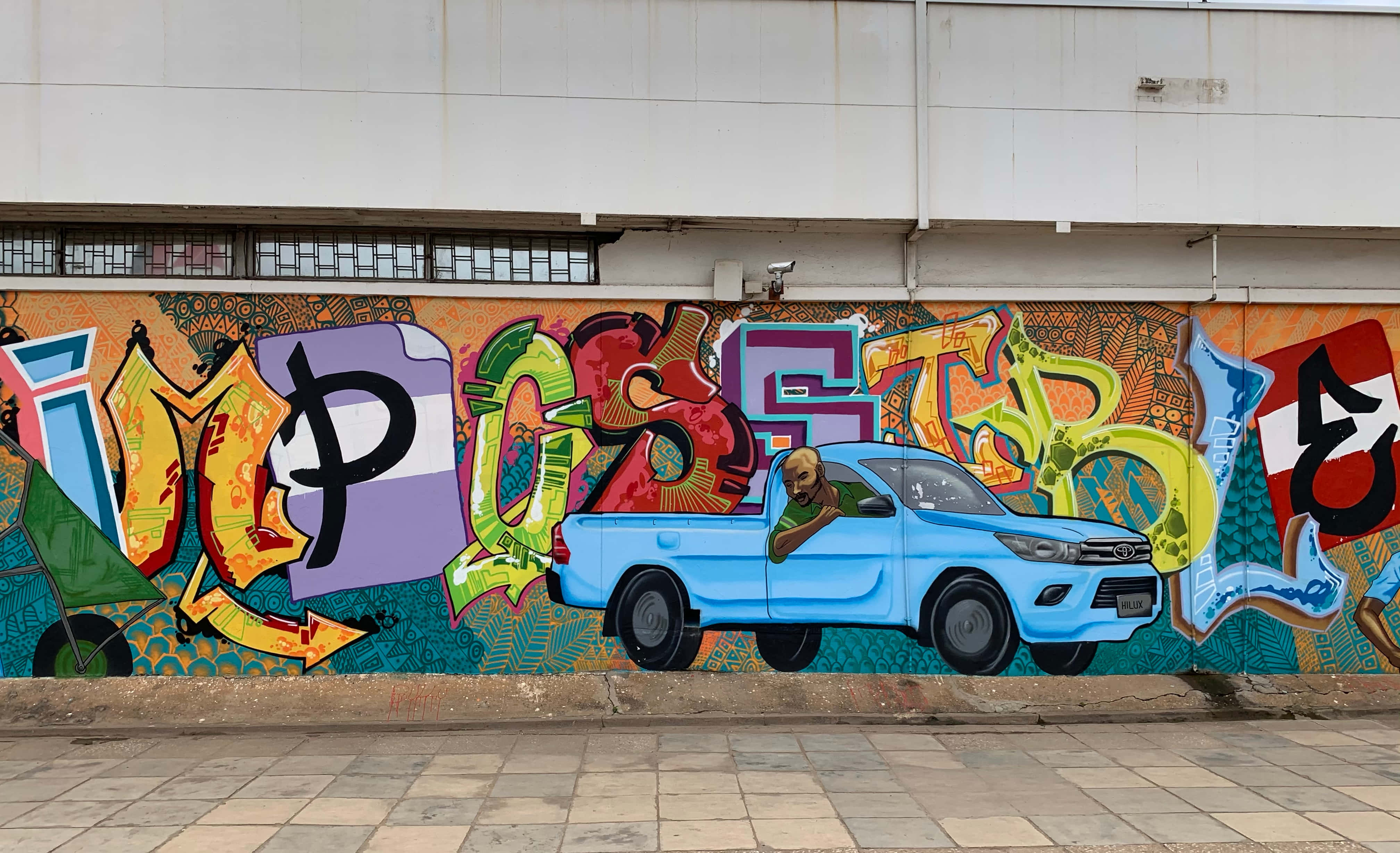 Graffiti Art 桌布 壁紙 — 一幅充滿活力的塗鴉壁畫，描繪一輛藍色皮卡車，車斗上有一名男子，周圍是混凝土牆上大膽多彩的字體。