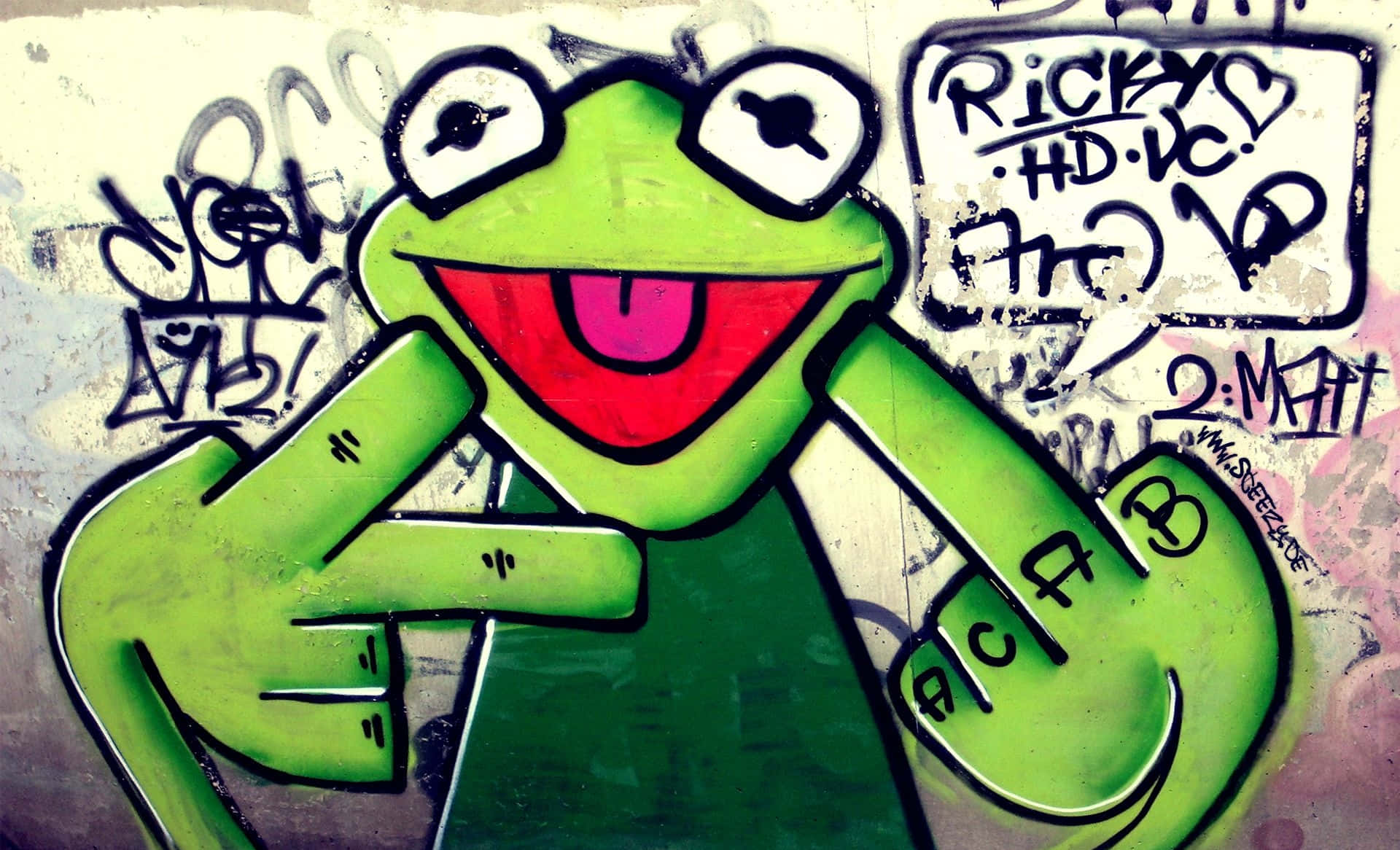 Graffiti Desktop 桌布 壁紙 — 一幅充滿活力的塗鴉壁畫，描繪了青蛙柯米特在風化的城市牆上咧嘴大笑並張開雙臂。
