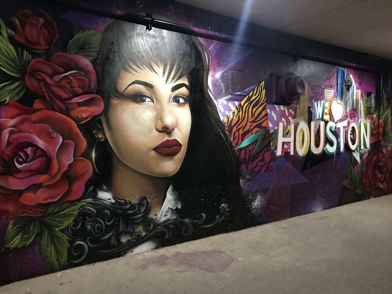 Selena Quintanilla 桌布 壁紙 — 一幅充滿活力的壁畫，描繪一位擁有鮮豔紅唇和玫瑰的女性，旁邊是紫色霓虹燈下的「I ❤️ HOUSTON」文字。