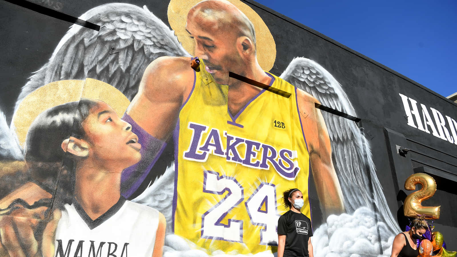籃球 桌布 壁紙 — 一幅充滿活力的壁畫描繪了柯比·布萊恩（Kobe Bryant）帶著天使翅膀和光環，在清澈的藍天下擁抱著一位身穿「Mamba」球衣的小女孩。