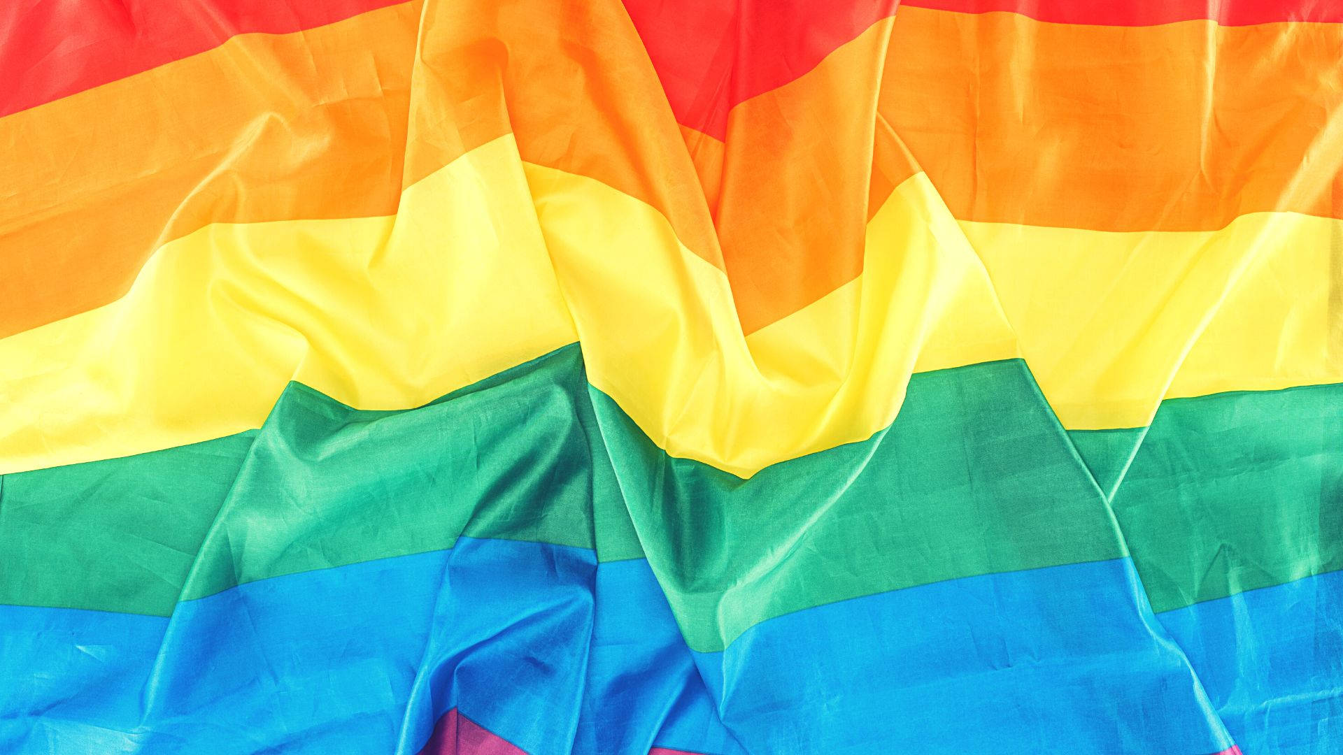 Subtle Lgbt 桌布 壁紙 — 一幅充滿活力的彩虹旗，布料褶皺流暢，在特寫鏡頭中捕捉光線。
