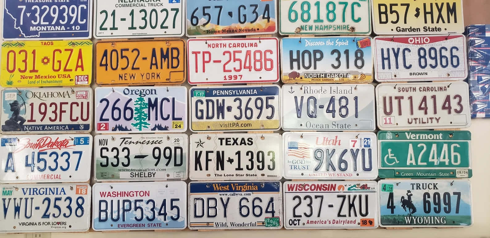 License Plate 桌布 壁紙 — 一幅充滿活力的拼貼畫，展示各種美國州份車牌掛在牆上，呈現多樣化的設計和標語。