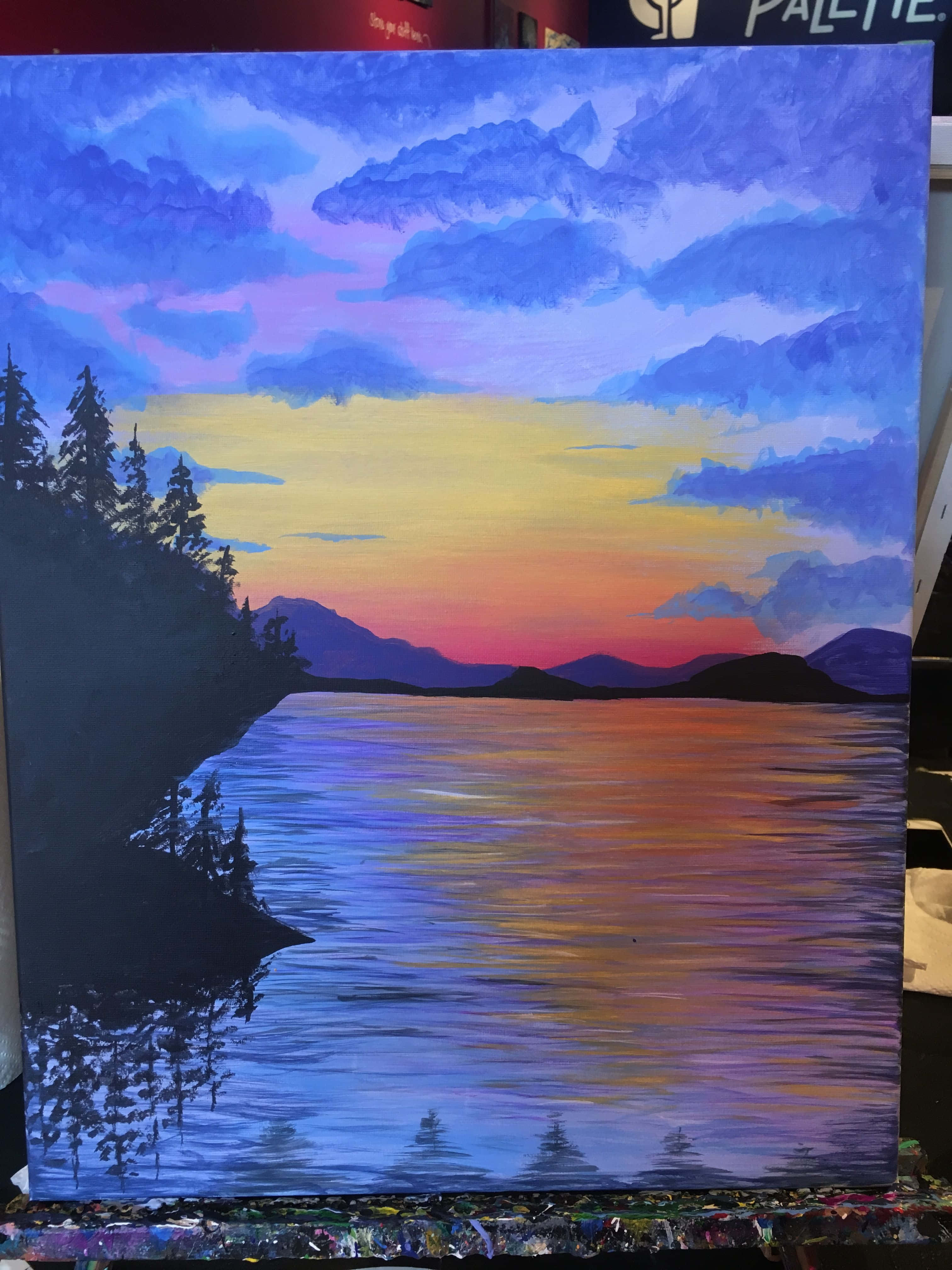 Painting 桌布 壁紙 — 一幅充滿活力的日落畫作，描繪了一個平靜的湖泊，倒映著紫色、橙色和黃色的天空，以及松樹和遠處山脈的剪影。