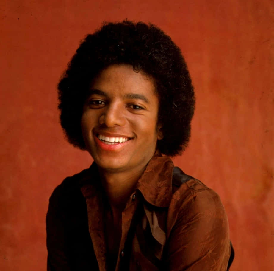 Young Michael Jackson 桌布 壁紙 — 一幅充滿活力的肖像，描繪一位微笑的年輕男子，擁有捲曲頭髮，背景為溫暖的陶土色。