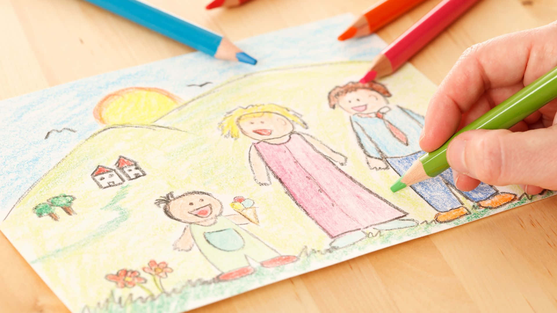 小孩動圖 桌布 壁紙 — 一幅兒童用彩色蠟筆畫的畫，畫中有微笑的家庭、山丘、太陽、房屋和花朵，正由成人手塗色。