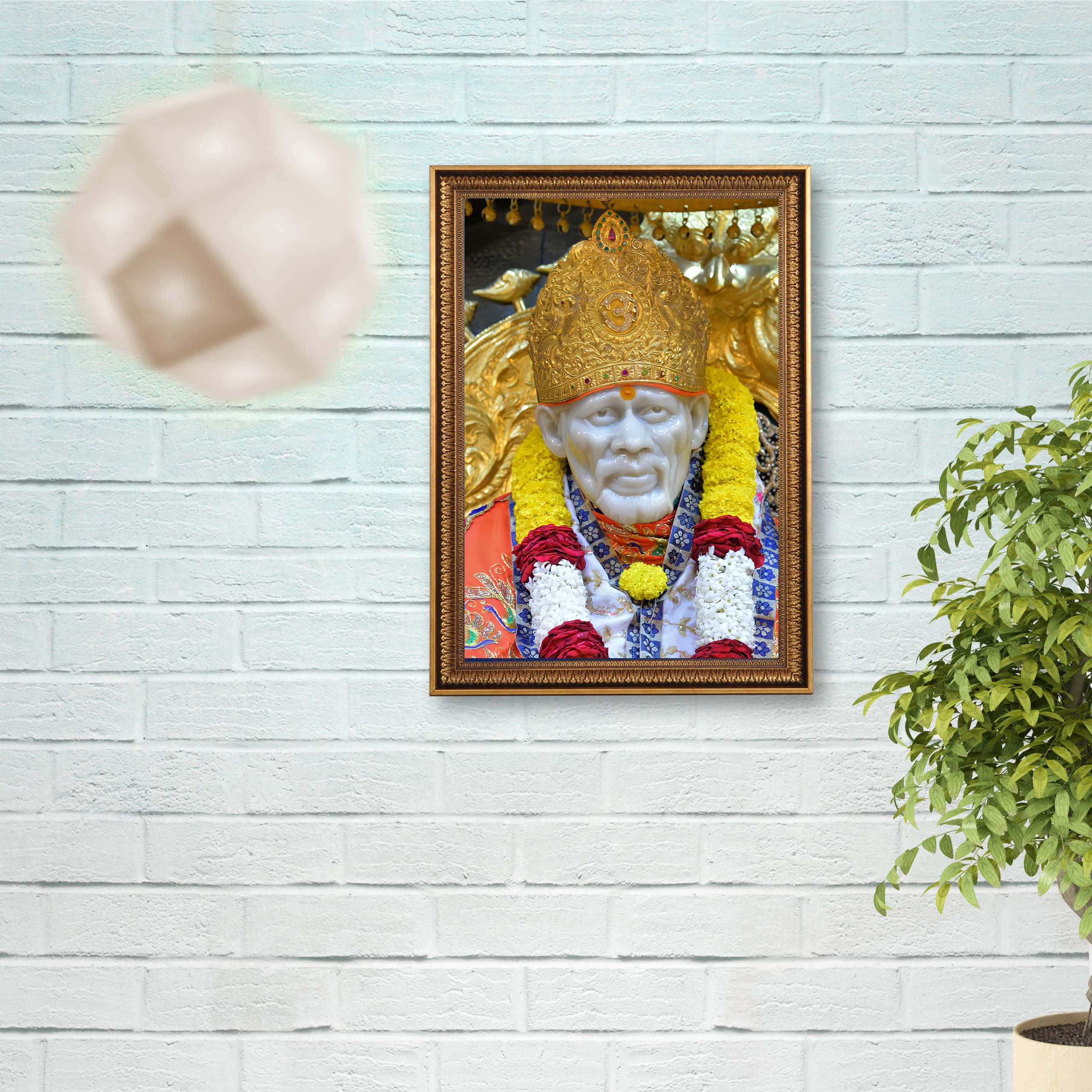 Indian 桌布 壁紙 — 一幅受人尊敬的印度教神祇的裱框肖像，戴著金色皇冠和花環，掛在白色磚牆上，旁邊有一盆盆栽植物。