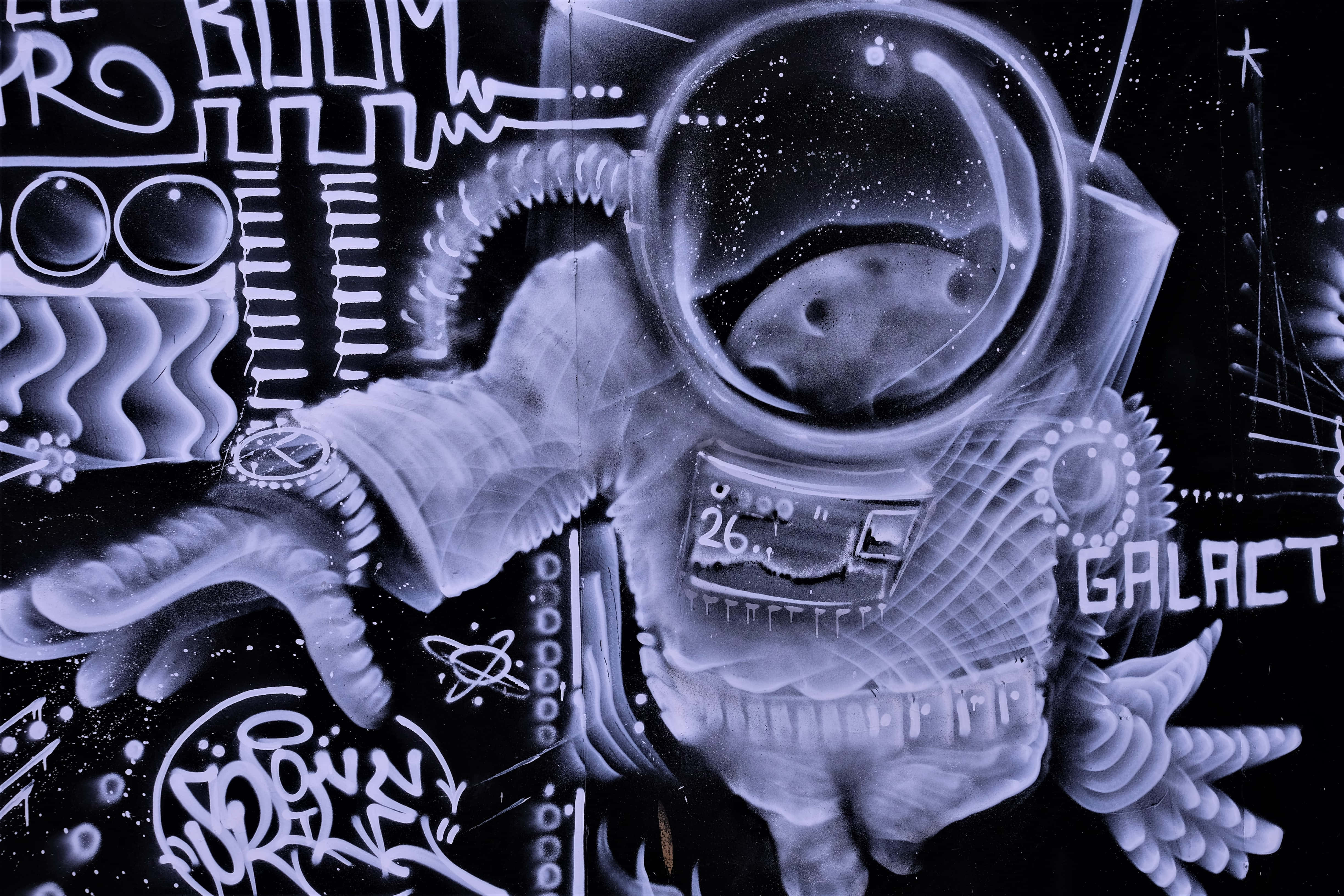 Space Art 桌布 壁紙 — 一幅單色塗鴉壁畫，描繪一個風格化的太空人，頭盔內有一個星系，周圍環繞著宇宙塗鴉和文字。