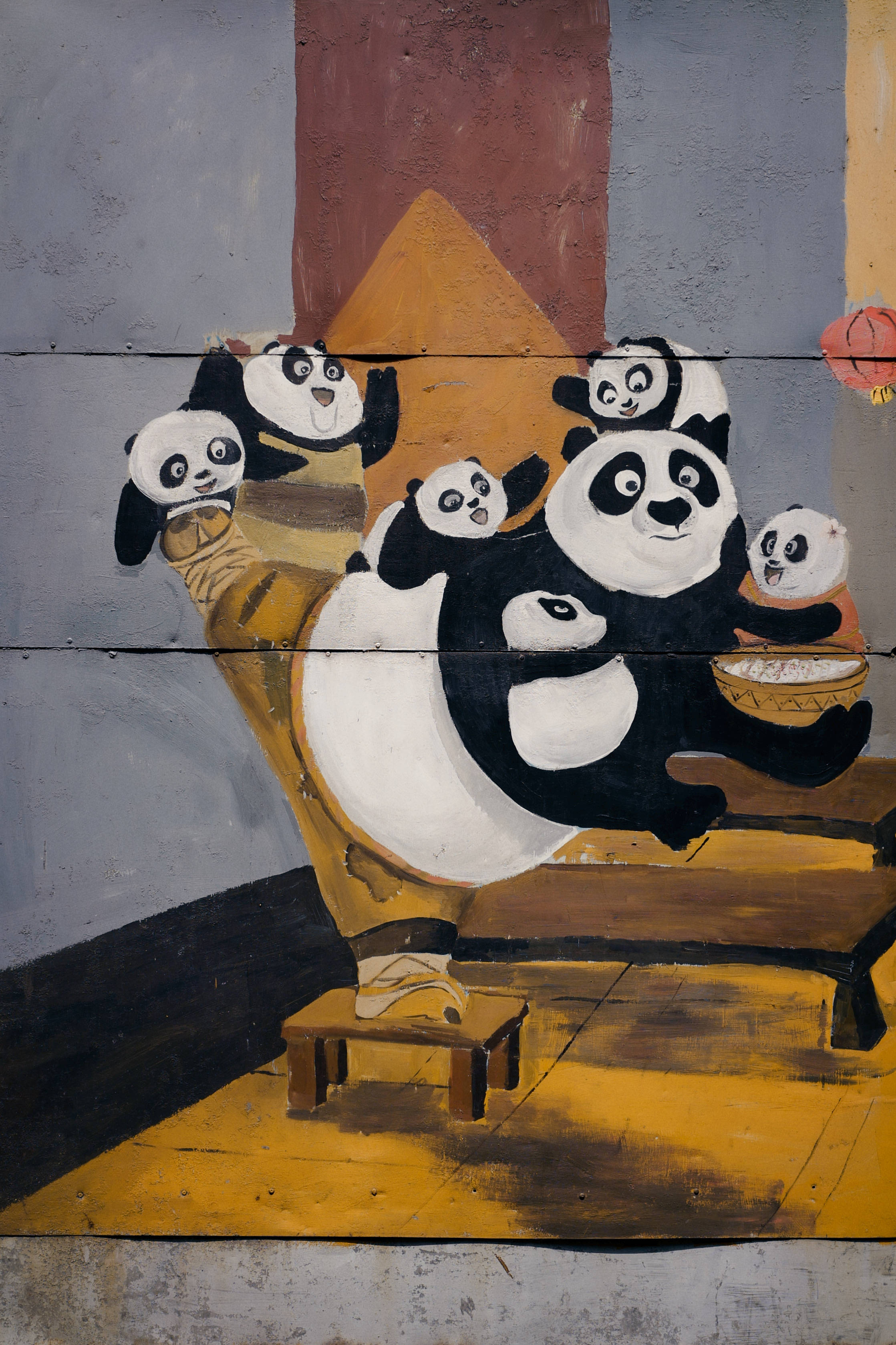 Cartoon 桌布 壁紙 — 一幅壁畫，描繪卡通熊貓圍著木桌分享食物，房間樸實，色調溫暖黃色。