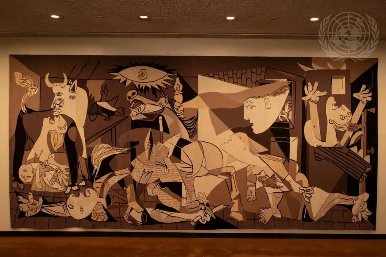 Picasso 桌布 壁紙 — 一幅大型抽象壁畫，以棕褐色調描繪扭曲的人物和幾何形狀，懸掛在溫暖天花燈下的畫廊中。