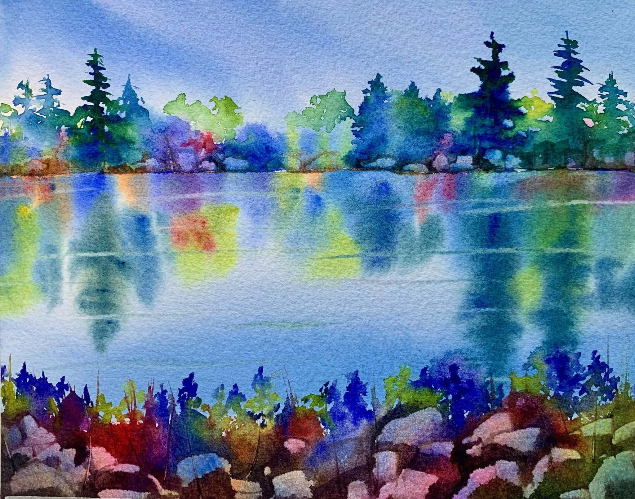 Watercolor 桌布 壁紙 — 一幅寧靜湖泊的水彩畫，映照出色彩繽紛的樹木和天空，前景有色彩鮮豔的岩石。