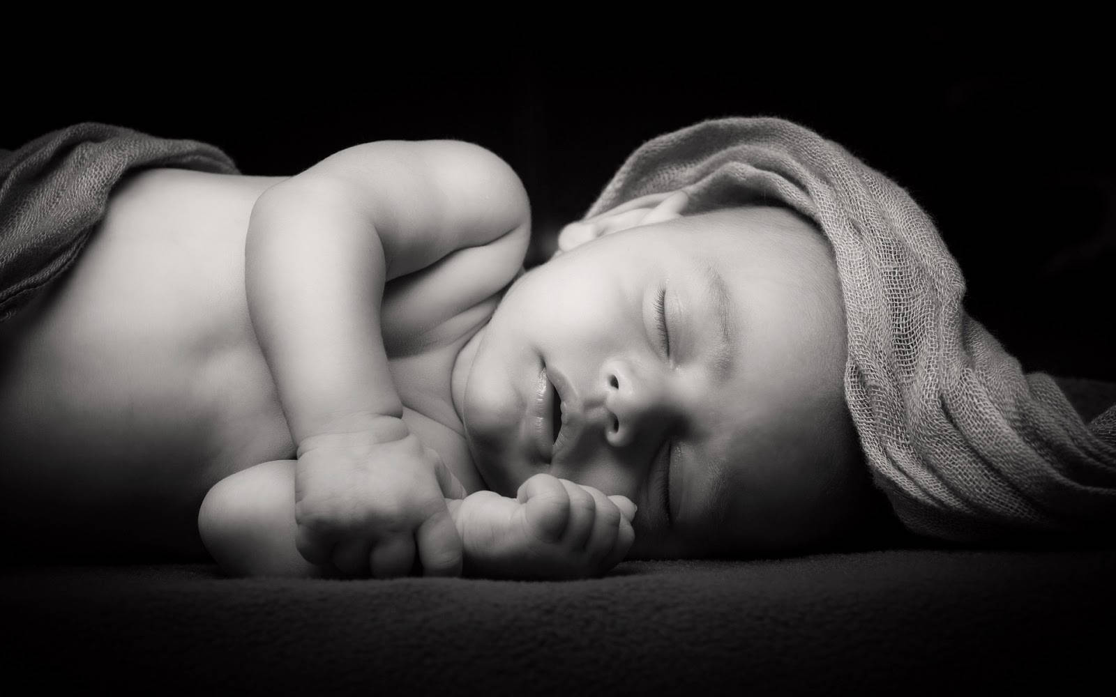 Baby 桌布 壁紙 — 一幅寧靜的黑白肖像，描繪一個在深色背景下用柔軟布料包裹的熟睡新生兒。