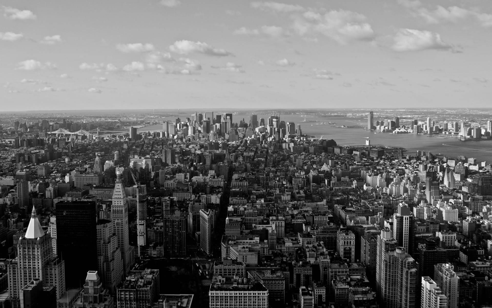 New York 桌布 壁紙 — 一幅廣闊的黑白航拍圖，展現密集的城市天際線，高樓大廈林立，天空明亮，雲朵散佈。