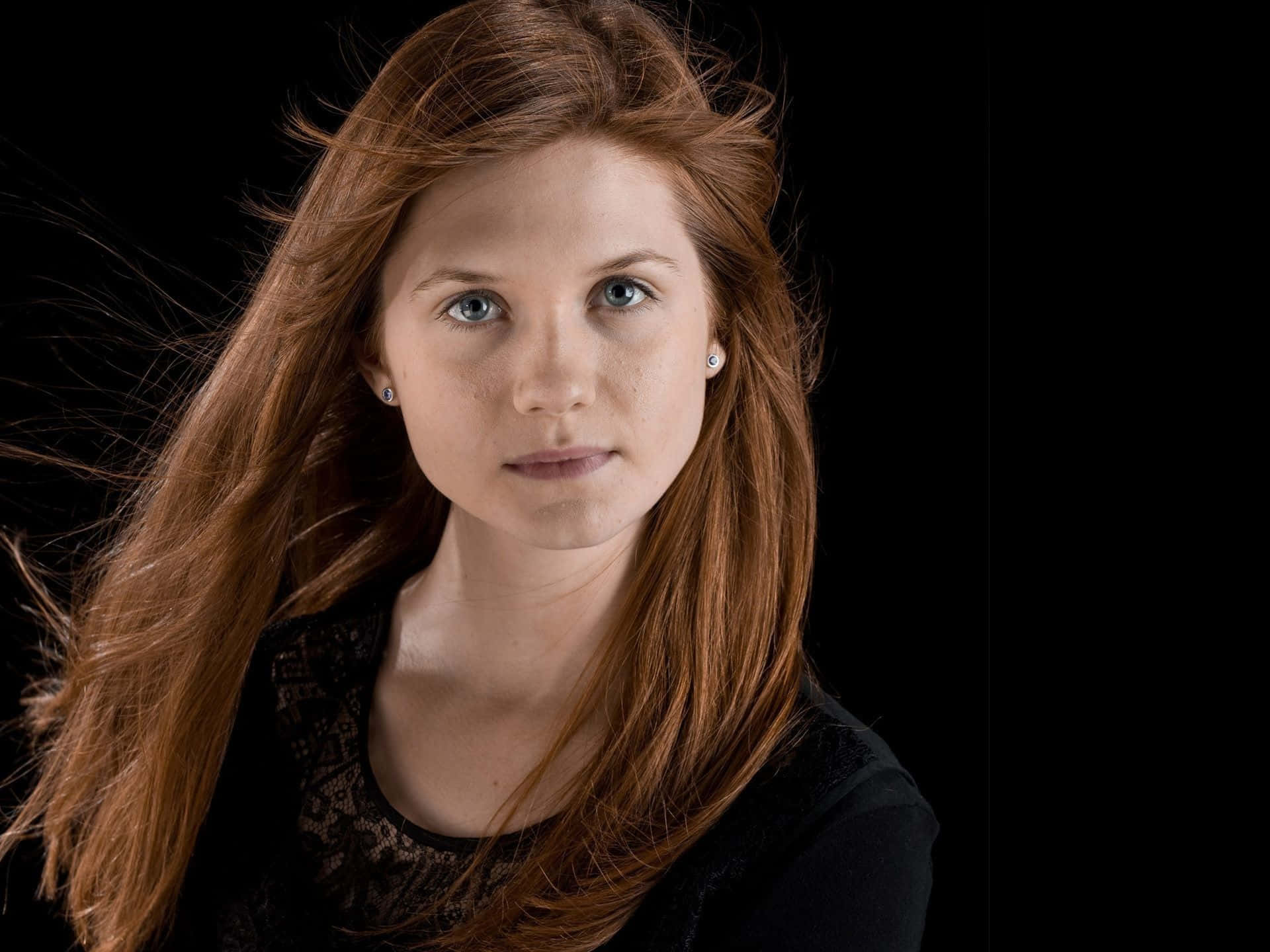 Ginny Weasley 桌布 壁紙 — 一幅引人注目的肖像，一位擁有火紅頭髮和銳利藍眼睛的女性，背景是純黑色。