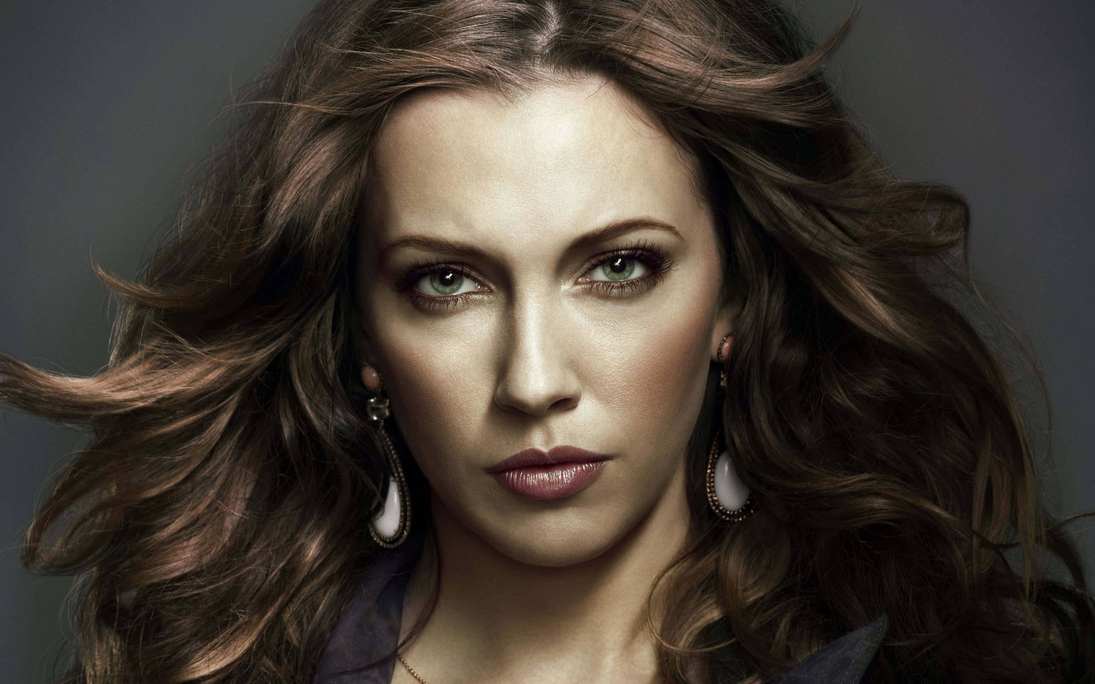 katie cassidy 桌布 壁紙 — 一幅引人注目的肖像，一位擁有飄逸棕色頭髮和強烈眼神的女性，背景為柔和的灰色。