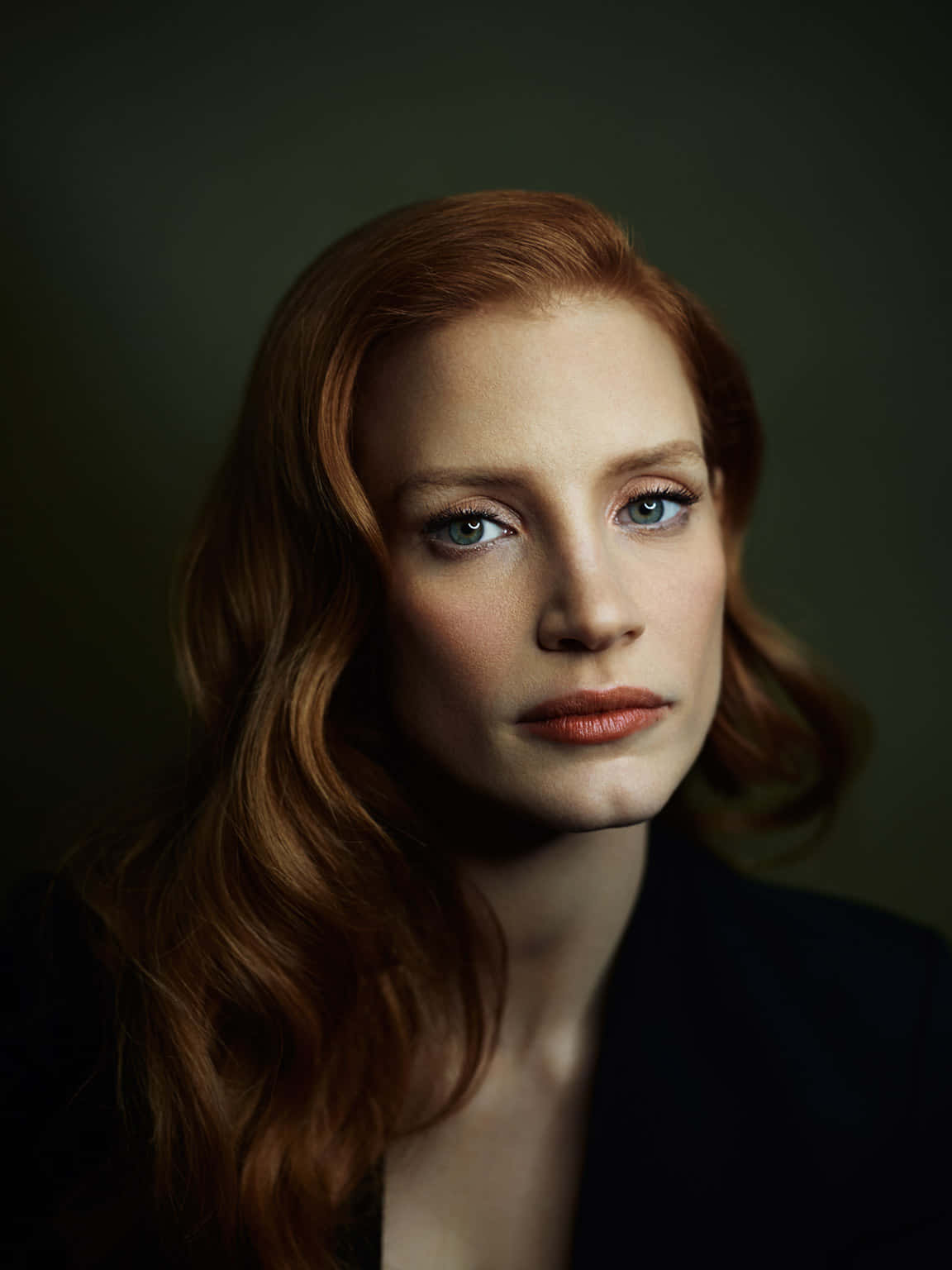 jessica chastain 桌布 壁紙 — 一幅引人注目的肖像，一位擁有鮮豔紅髮和銳利藍眼睛的女性，背景為深色柔和色調。