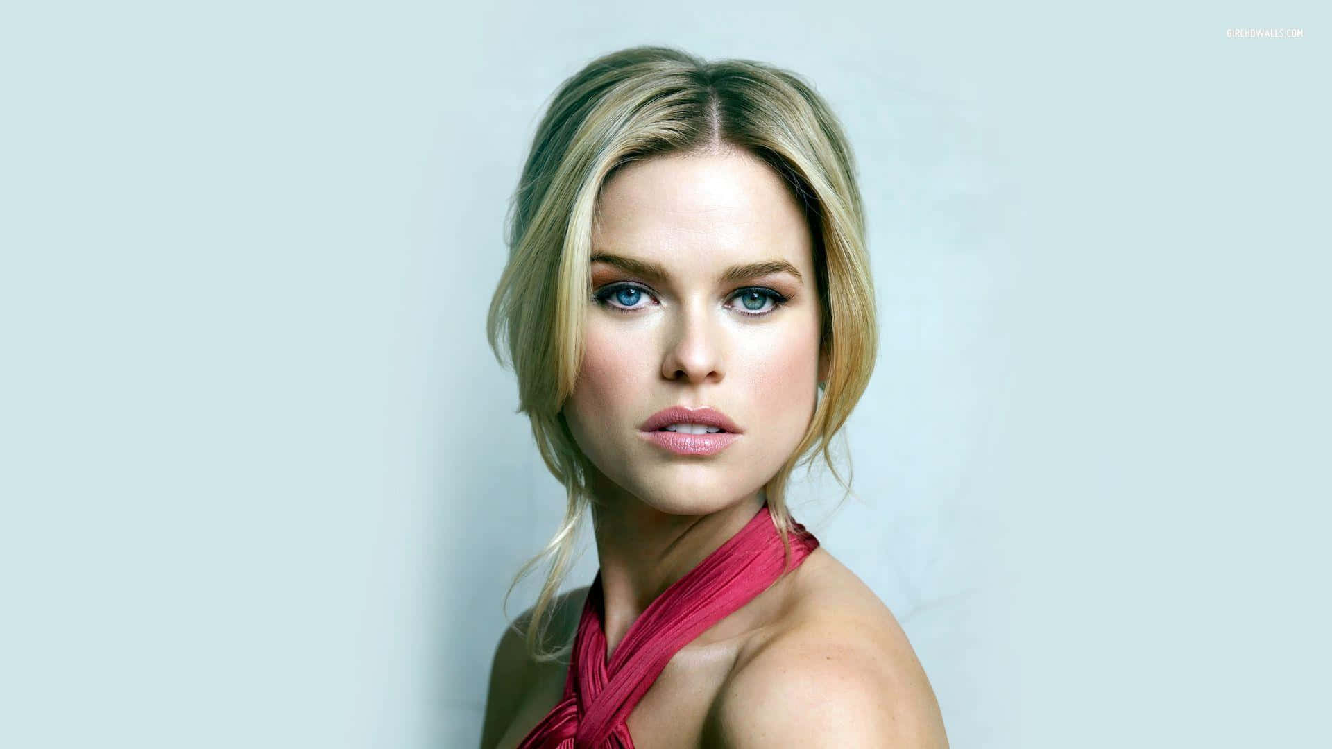 alice eve 桌布 壁紙 — 一幅引人注目的肖像，一位金髮碧眼、身穿紅色掛頸上衣的女性，背景是柔和的淺藍色。
