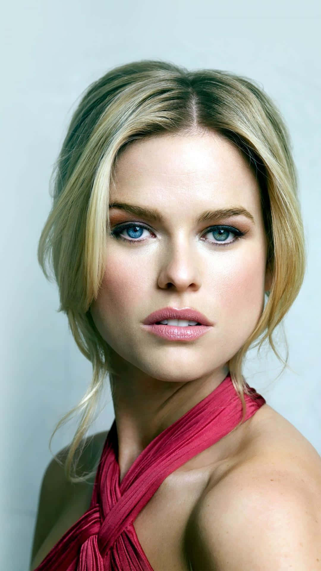 alice eve 桌布 壁紙 — 一幅引人注目的肖像，一位金髮碧眼、眼神銳利的女性，穿著鮮紅色掛頸上衣，背景是柔和的灰色。