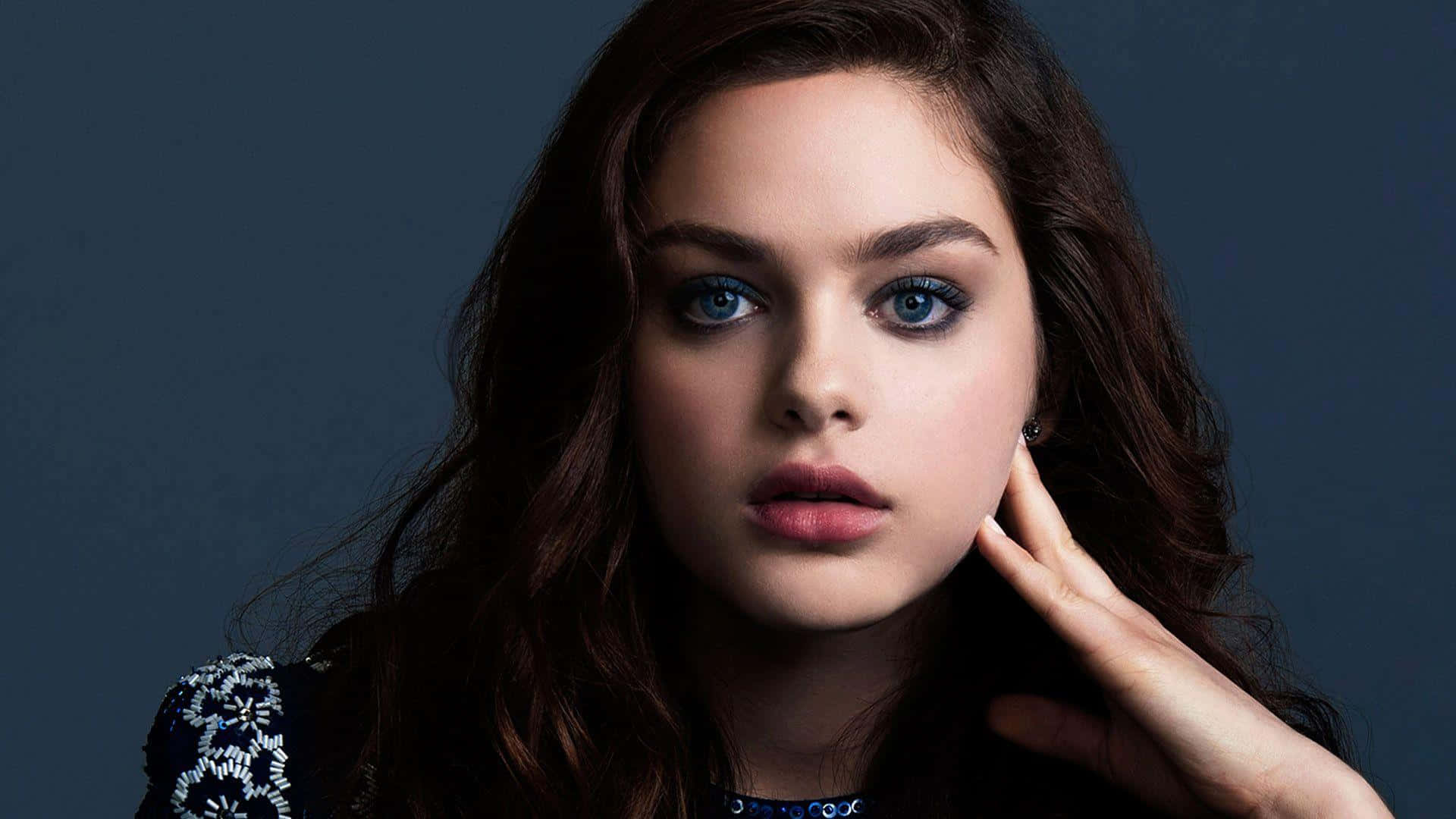 Odeya Rush 桌布 壁紙 — 一幅引人注目的肖像，描繪一位年輕女性，擁有鮮明的藍色眼睛和深色頭髮，在柔和的藍色背景前直視鏡頭。
