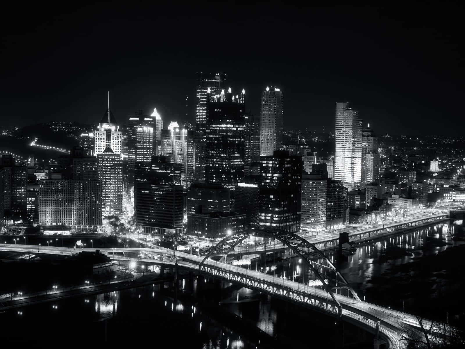 Black And White Cityscape 桌布 壁紙 — 一幅引人注目的黑白夜景城市天際線，燈火通明的摩天大樓和橋樑倒映在水中。