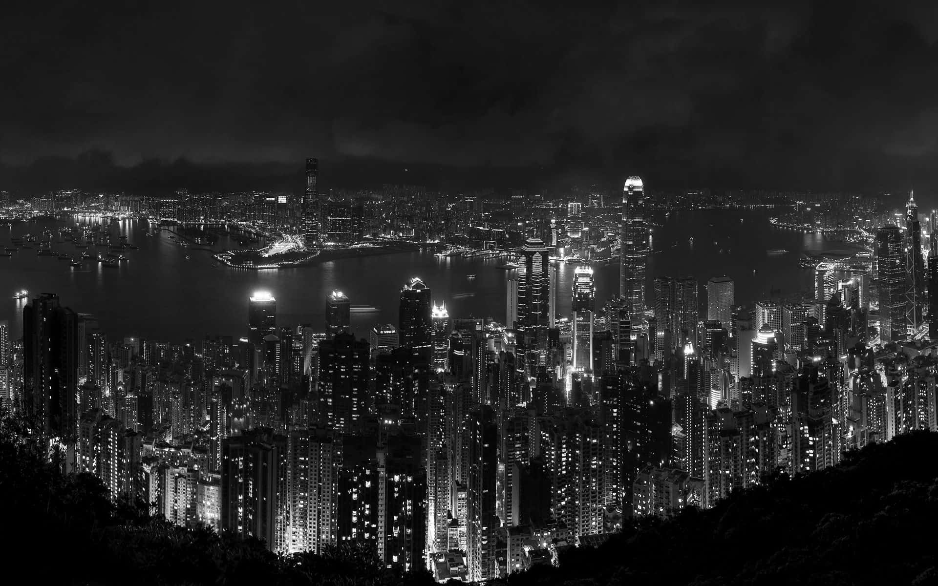 桌布 壁紙 — 一幅引人注目的黑白空拍圖，展現了夜晚密集燈光的城市景觀，港口和遠處的山脈在黑暗的天空下。