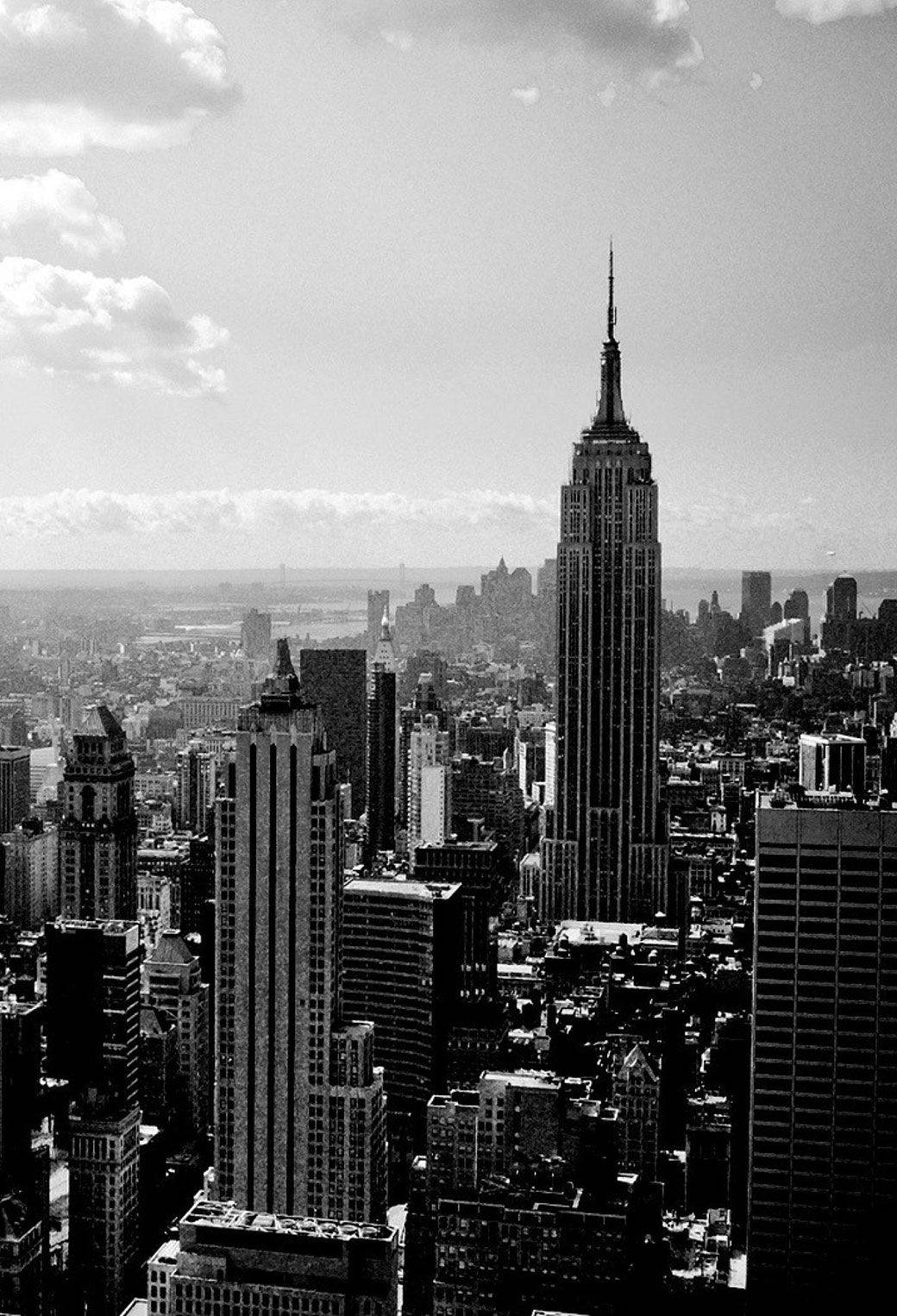 manhattan 桌布 壁紙 — 一幅引人注目的黑白空拍圖，帝國大廈在部分多雲的天空下聳立於紐約市密集的城市天際線之上。