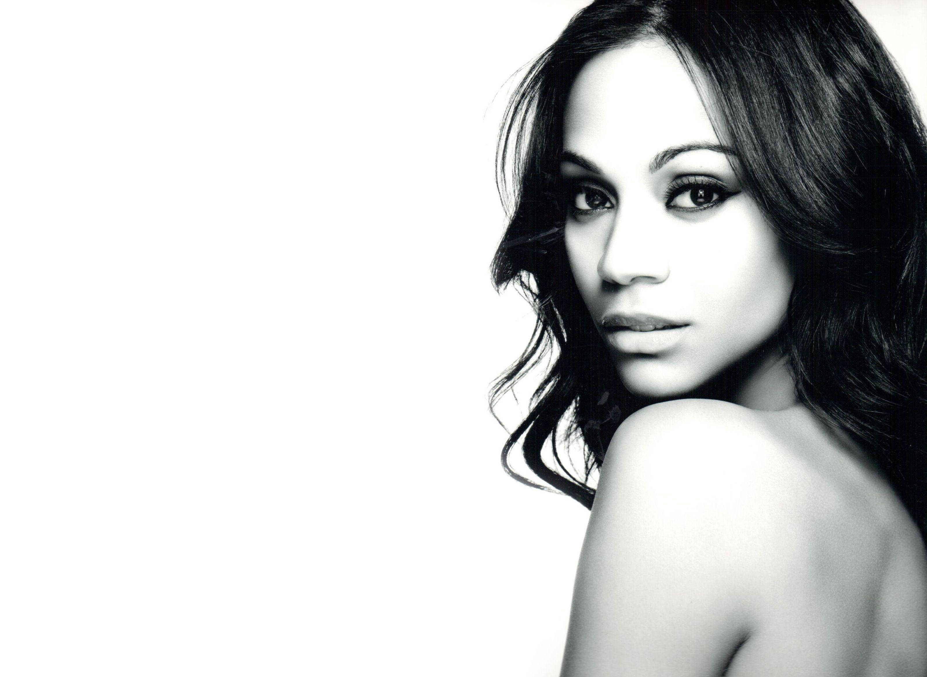 Zoe Saldana 桌布 壁紙 — 一幅引人注目的黑白肖像，一位深色頭髮的女性在純白背景下直視鏡頭。