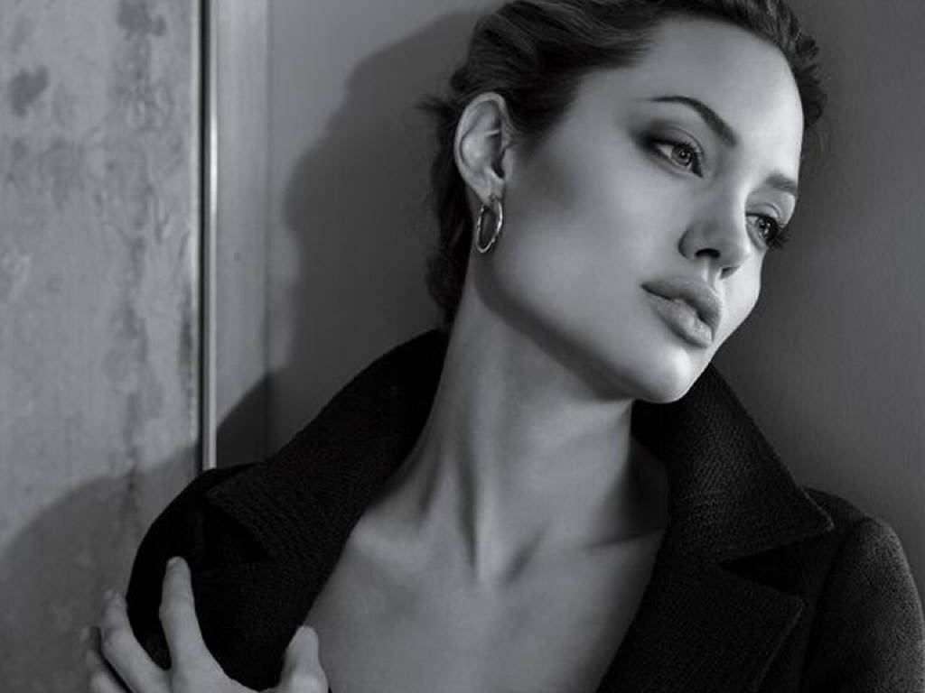 Angelina 桌布 壁紙 — 一幅引人注目的黑白肖像，一名女子靠在牆上，柔和的光線凸顯她沉思的表情。