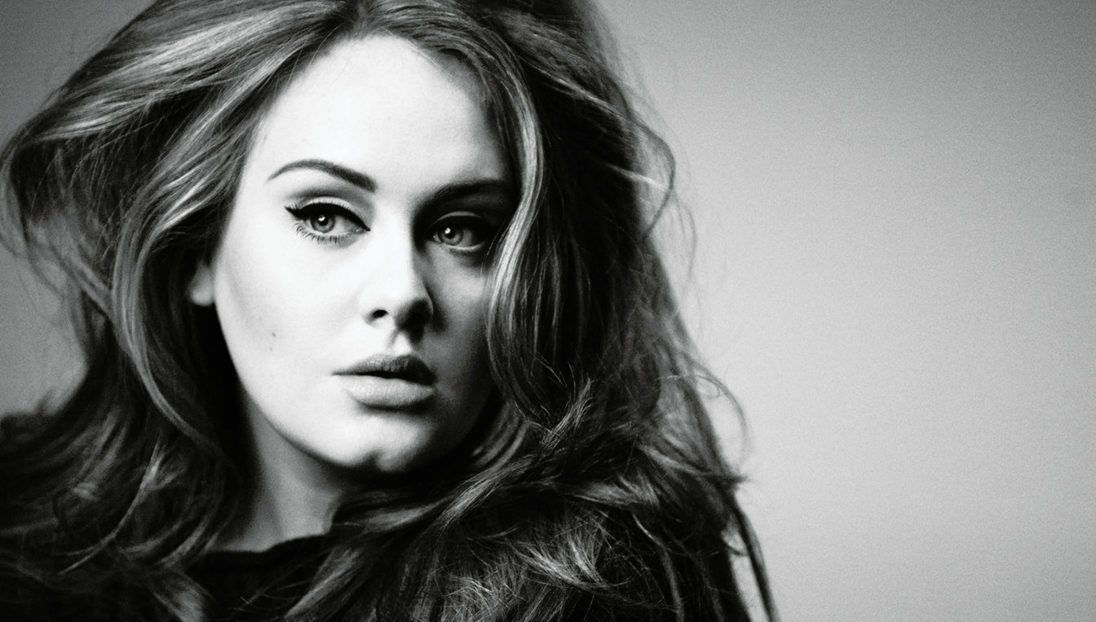 Adele 桌布 壁紙 — 一幅引人注目的黑白肖像照，捕捉一位女性強烈的眼神和飄逸的頭髮，背景簡潔。