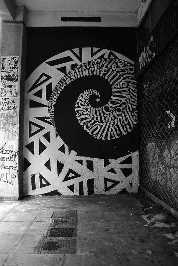 Black And White Graffiti 桌布 壁紙 — 一幅引人注目的黑白螺旋幾何圖案壁畫，覆蓋在粗糙的城市小巷牆上。