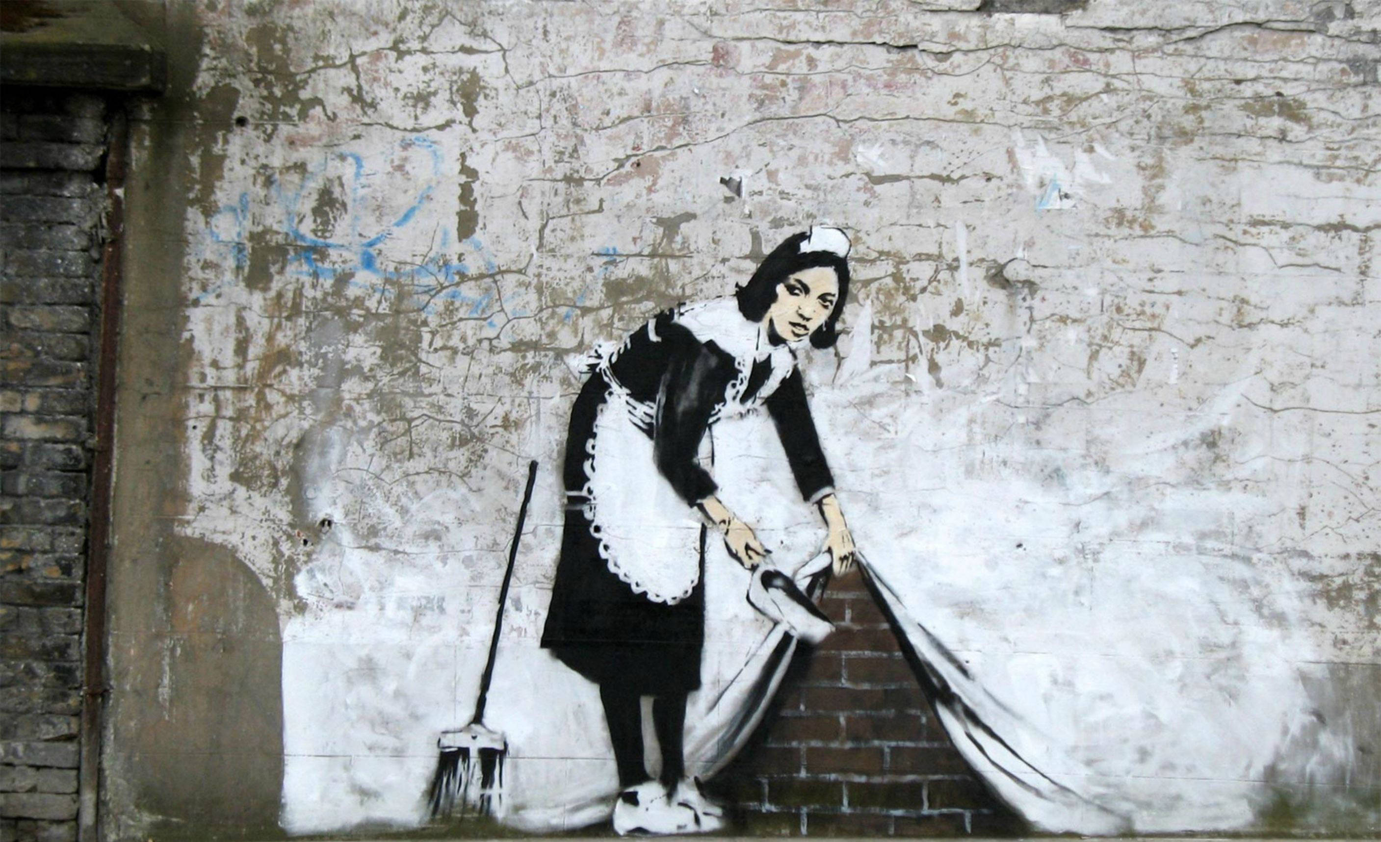 Banksy 桌布 壁紙 — 一幅引人注目的黑白街頭藝術壁畫，描繪一名穿著傳統制服的女傭用掃帚清掃牆壁。