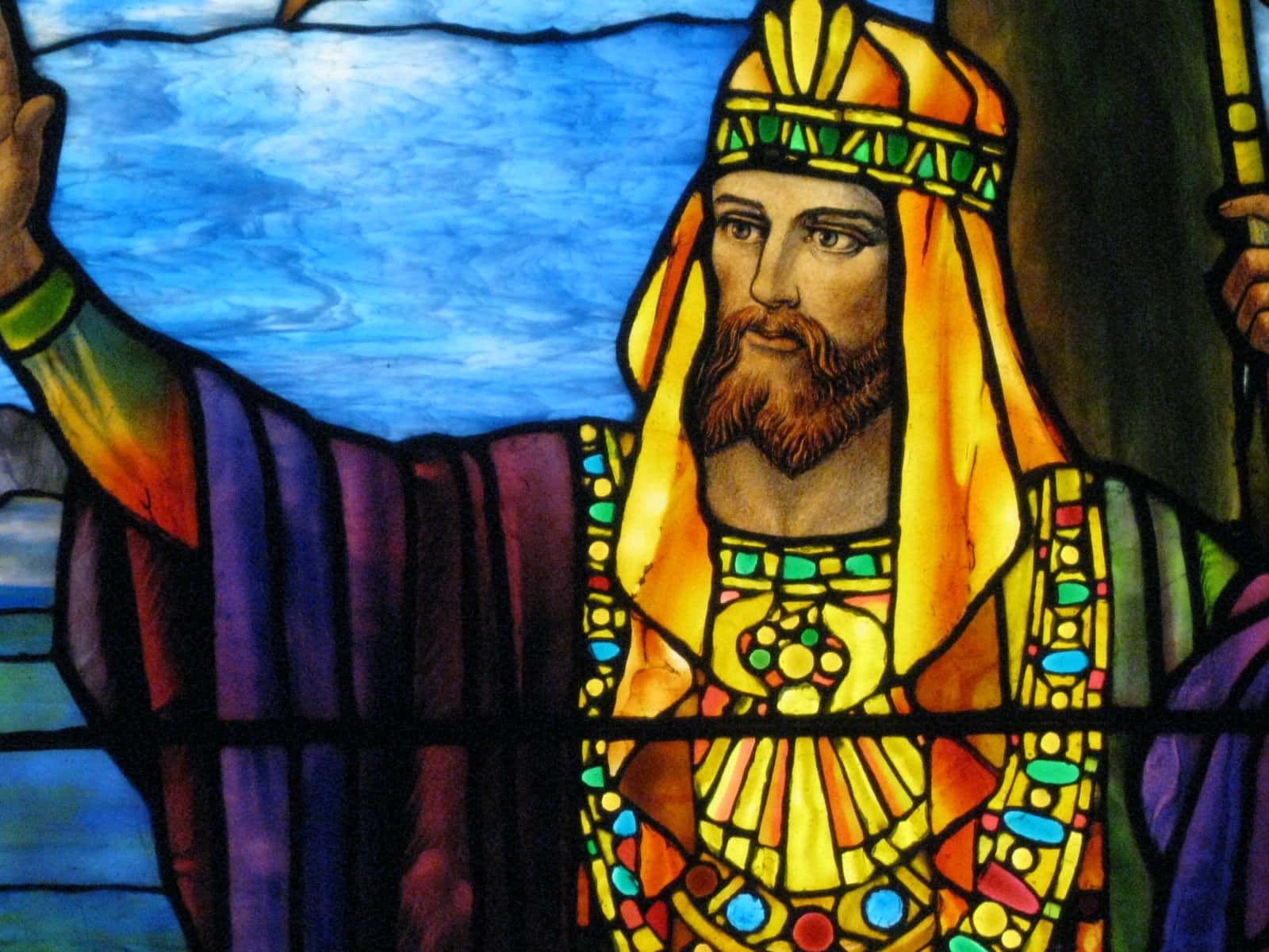 King Solomon 桌布 壁紙 — 一幅彩色玻璃描繪，一位鬍鬚國王身穿金色長袍、頭戴王冠，在藍天背景下舉起手。