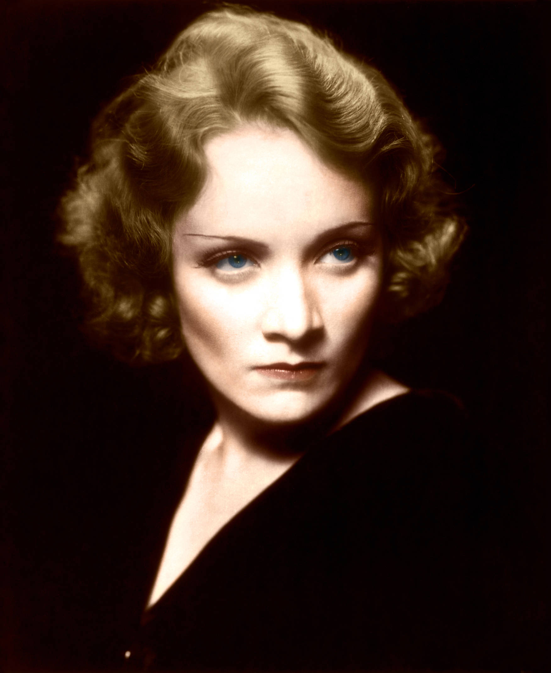 Marlene Dietrich 桌布 壁紙 — 一幅復古工作室肖像，一位擁有引人注目的藍色眼睛和柔軟捲髮的女性，背景為深色。