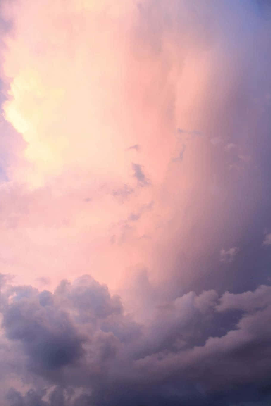 美學雲朵 桌布 壁紙 — 一幅戲劇性的天空，塗上柔和的粉紅、紫色和黃色調，陽光穿過蓬鬆的雲層。