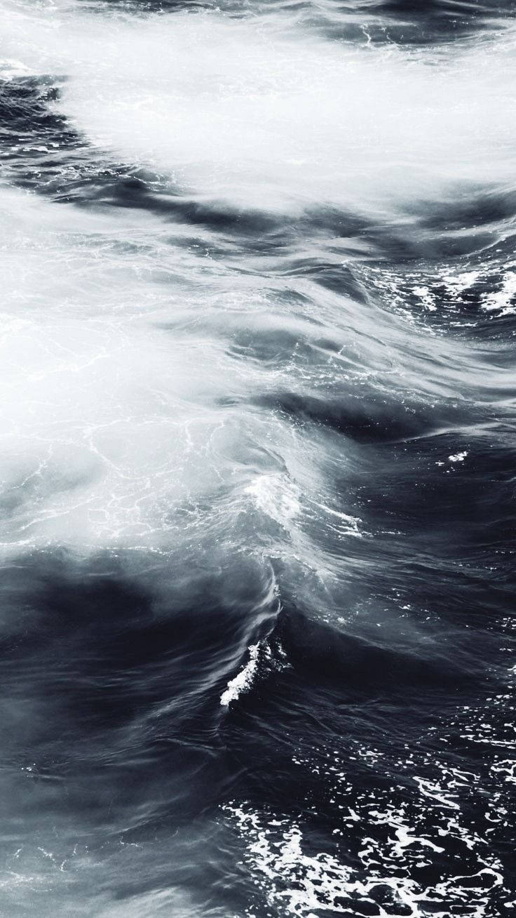 Black And White iPhone 桌布 壁紙 — 一幅戲劇性的空拍圖，展示翻騰的海浪，深藍色的海水和泡沫狀的白色浪花在動態運動中旋轉。