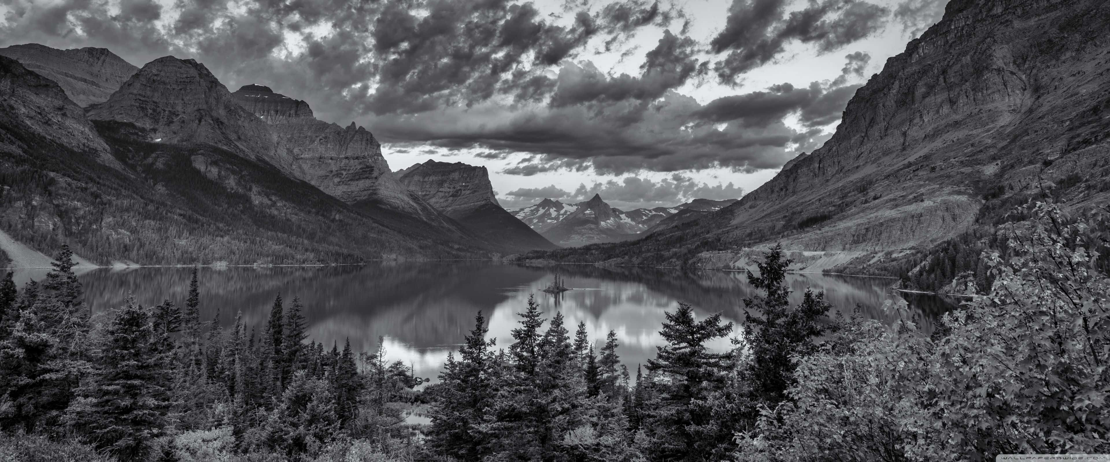 Apple 3840x1600 桌布 壁紙 — 一幅戲劇性的黑白全景圖，展現山間湖泊倒映著高聳的山峰和暴風雲。