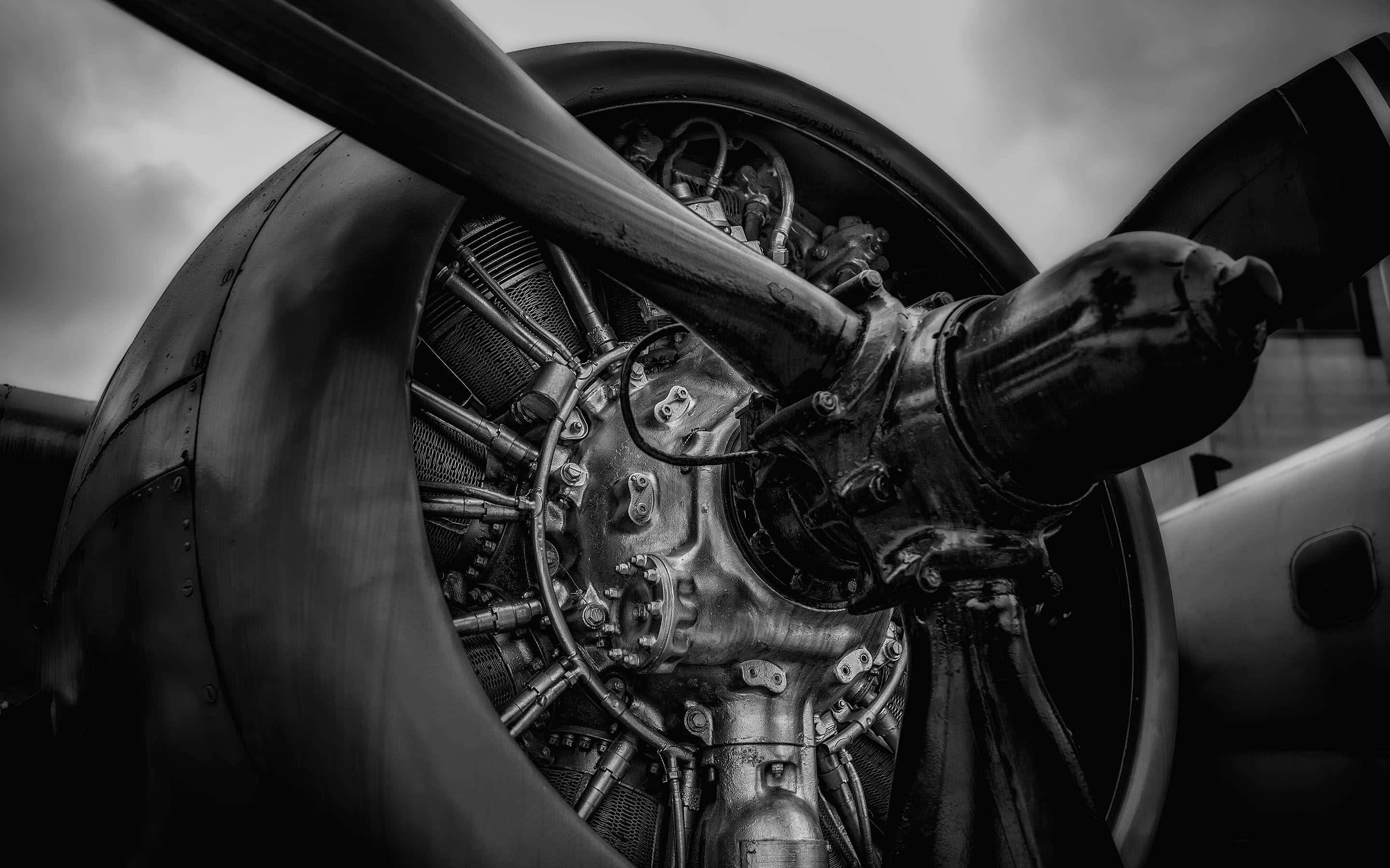 Jet Engine 桌布 壁紙 — 一幅戲劇性的黑白特寫，展示復古飛機引擎與螺旋槳葉片，背景為多雲天空。