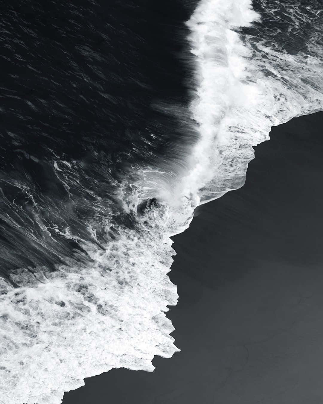Black And White Ocean 桌布 壁紙 — 一幅戲劇性的黑白航拍圖，展示破碎的海浪，深色海水與白色泡沫形成強烈對比。