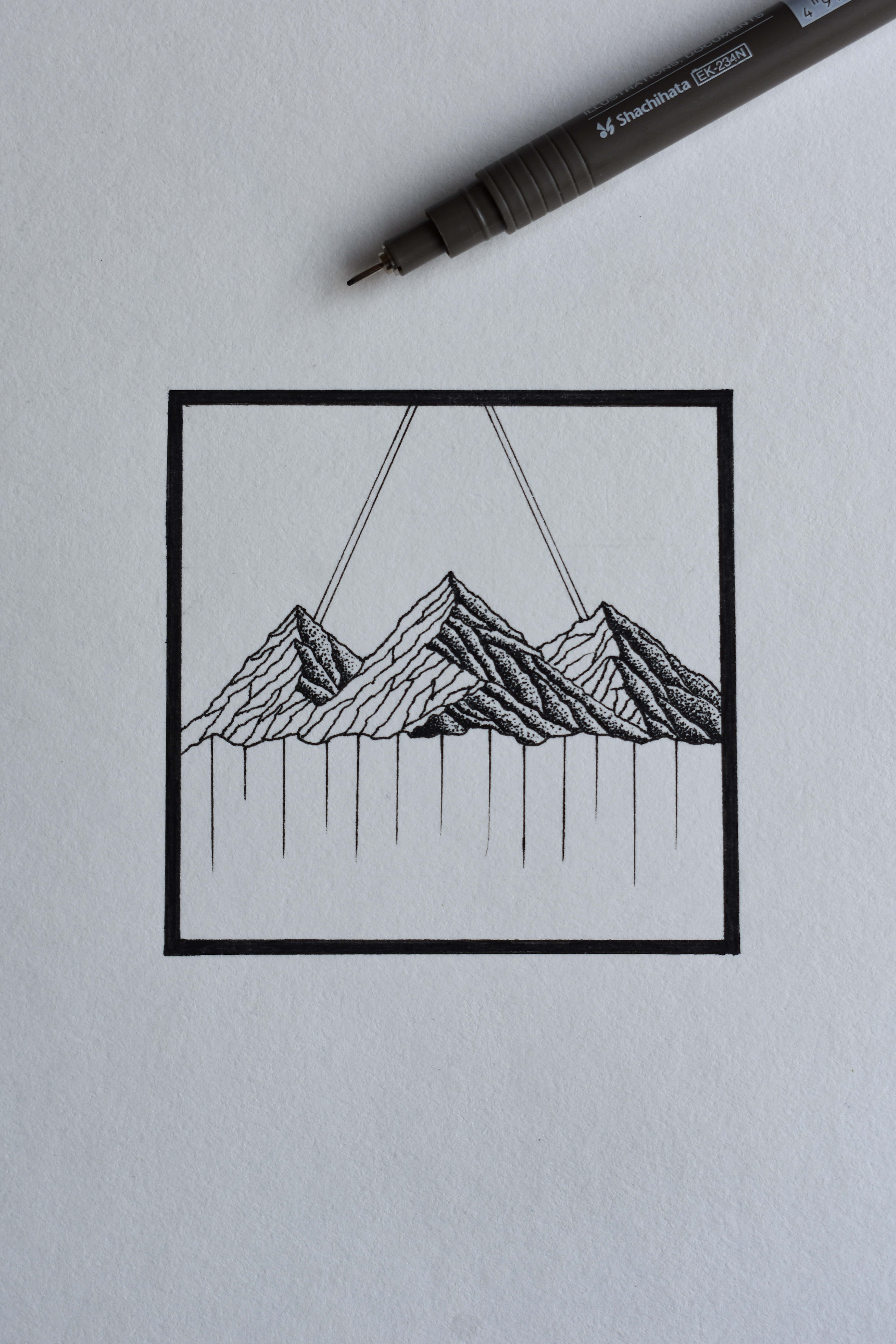 Black And White Drawings 桌布 壁紙 — 一幅極簡風格的黑色墨水畫，描繪了用繩子懸掛在方形框架內的山脈，畫在白色紙上，附近有一支筆。